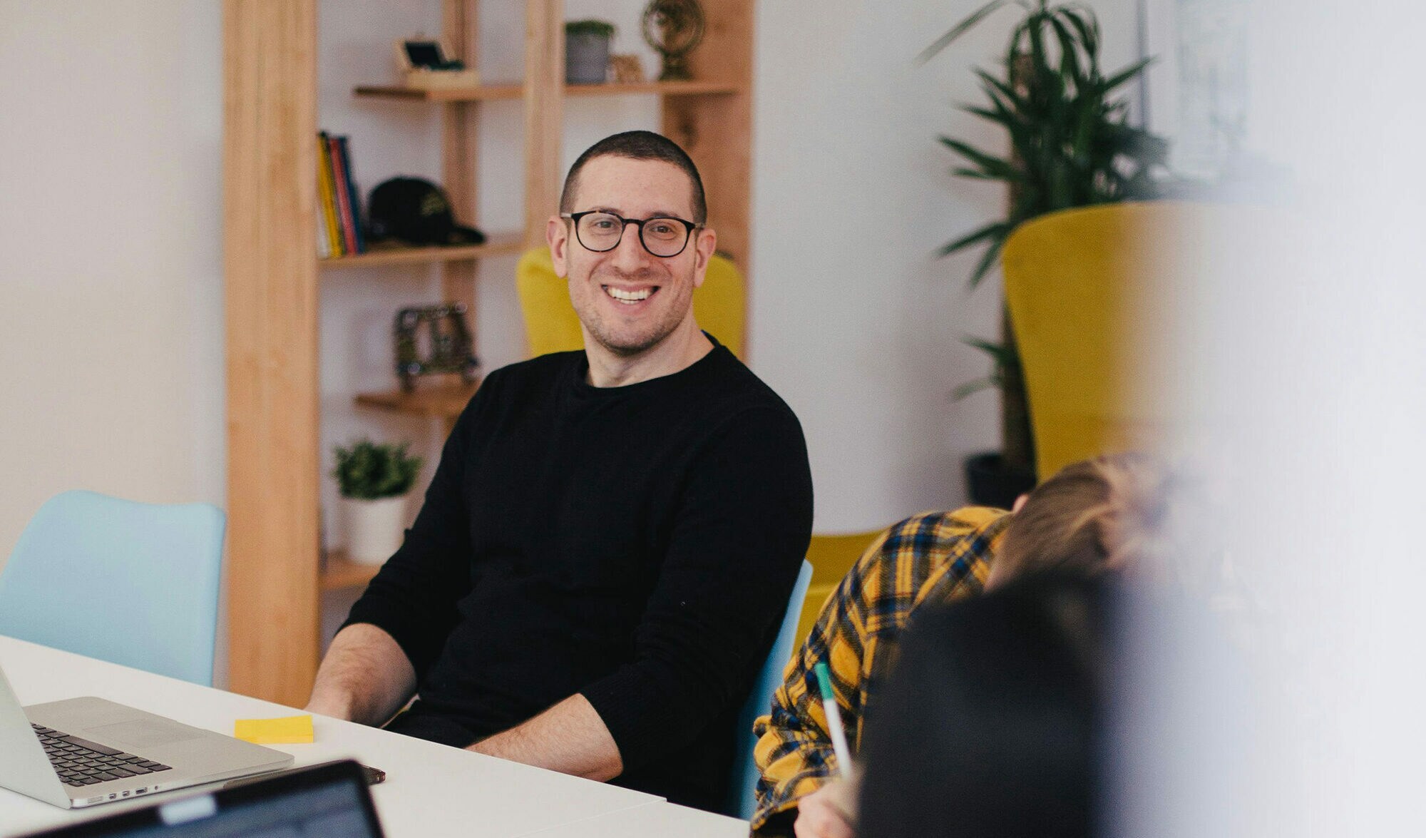 Laterale Führung: der Schlüssel für gemeinsamen Erfolg Ein junger Mann lächelt bei der Arbeit mit Kolleg:innen.