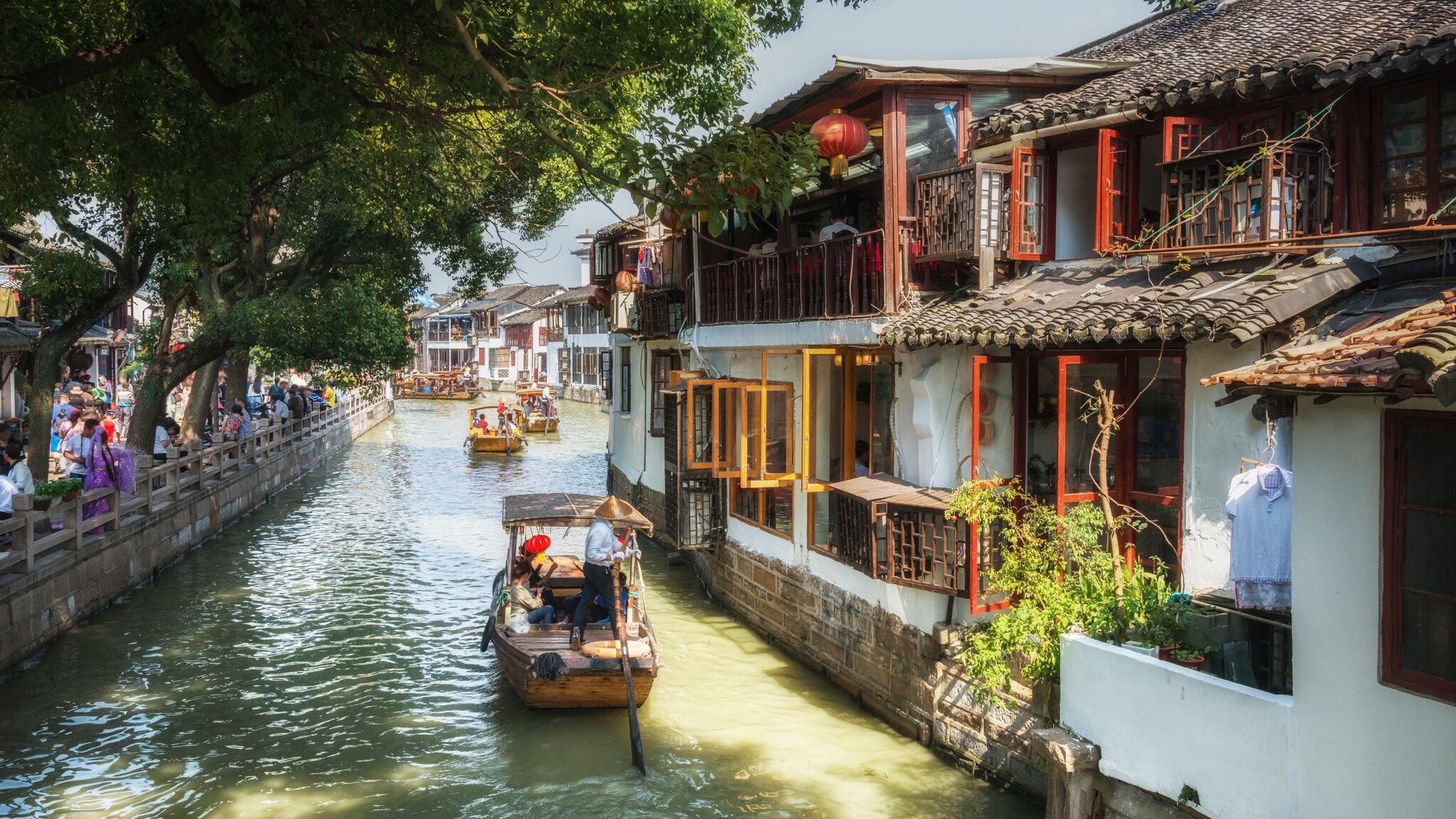 Boote mit Personen mit asiatischem Kegelhut auf einem Kanal entlang einer Häuserfront, links Menschenmenge auf einer Promenade. Boote mit Personen mit asiatischem Kegelhut auf einem Kanal entlang einer Häuserfront, links Menschenmenge auf einer Promenade.