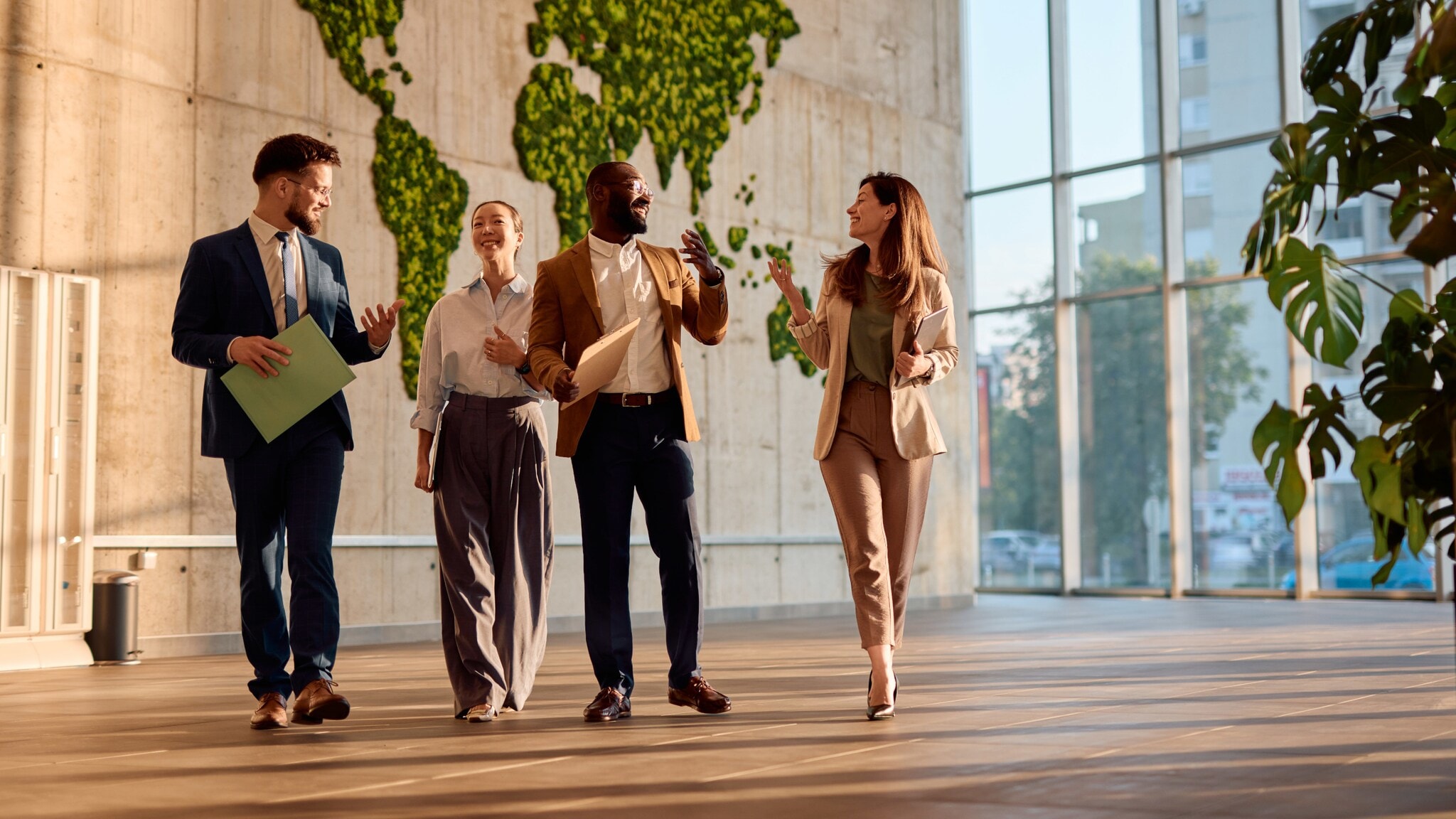 Vier Personen in Business-Outfits kommunizieren nebeneinander gehend in einem Foyer. Vier Personen in Business-Outfits kommunizieren nebeneinander gehend in einem Foyer.