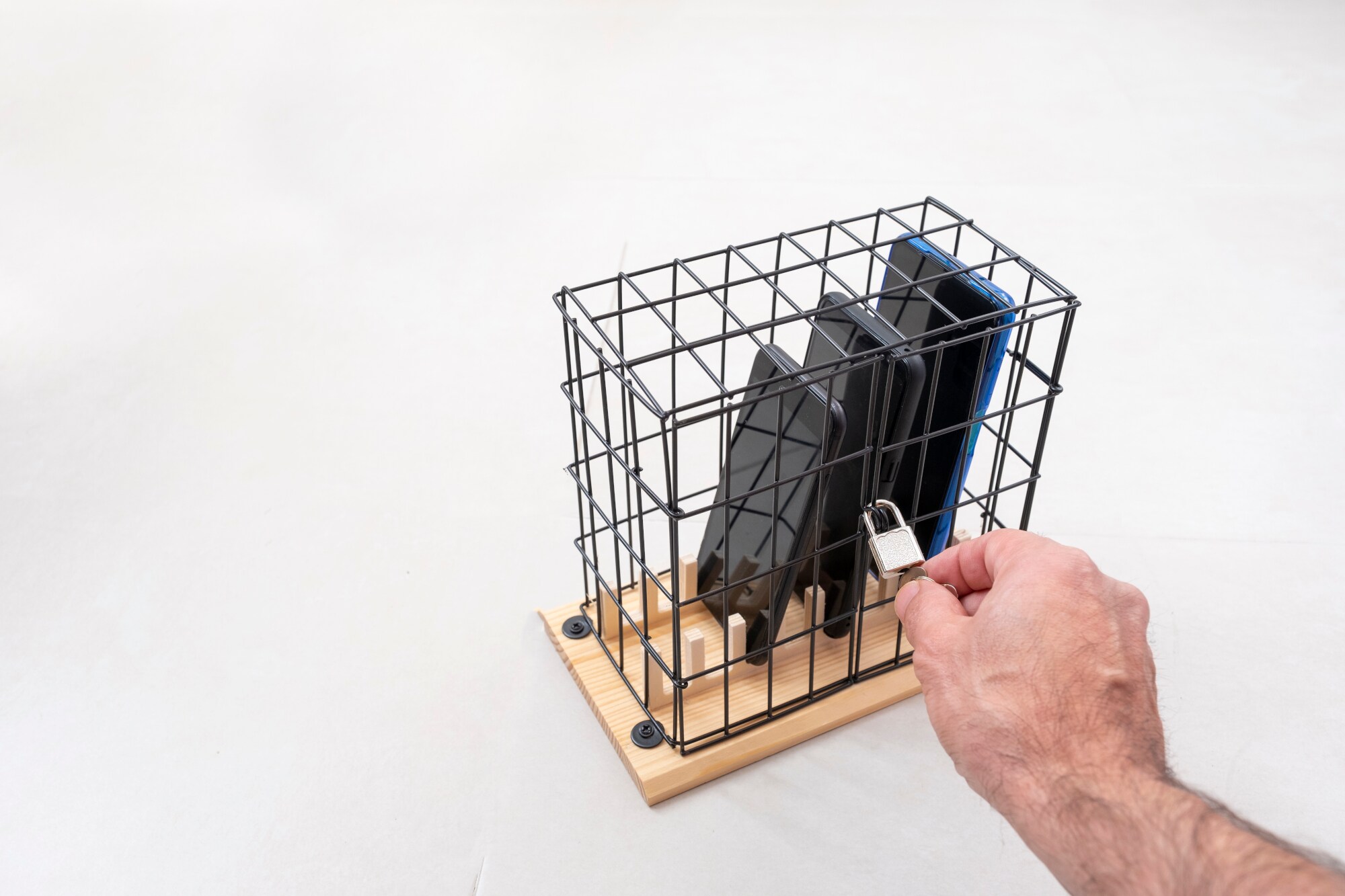 Eine Hand steckt einen Schlüssel in ein Schloss an einem kleinen Käfig mit drei Mobiltelefonen