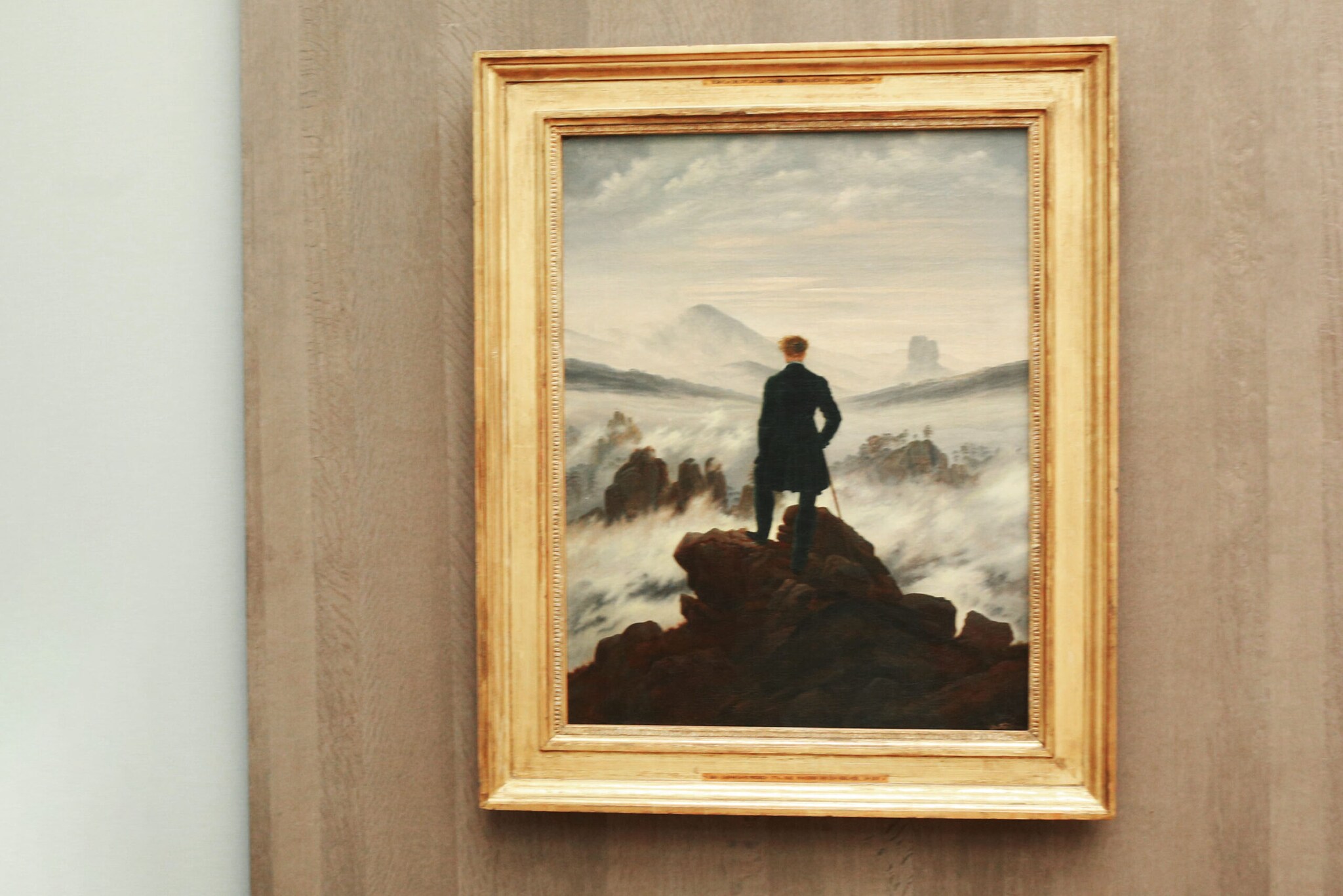 Das Gemälde Der Wanderer über dem Nebelmeer in einem goldenen Rahmen an der Wand Das Gemälde Der Wanderer über dem Nebelmeer in einem goldenen Rahmen an der Wand