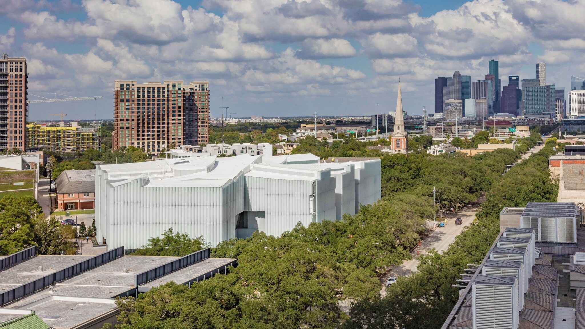 Ein modernes, weißes Museumsgebäude in einem Park in einer Stadt vor einer Skyline.