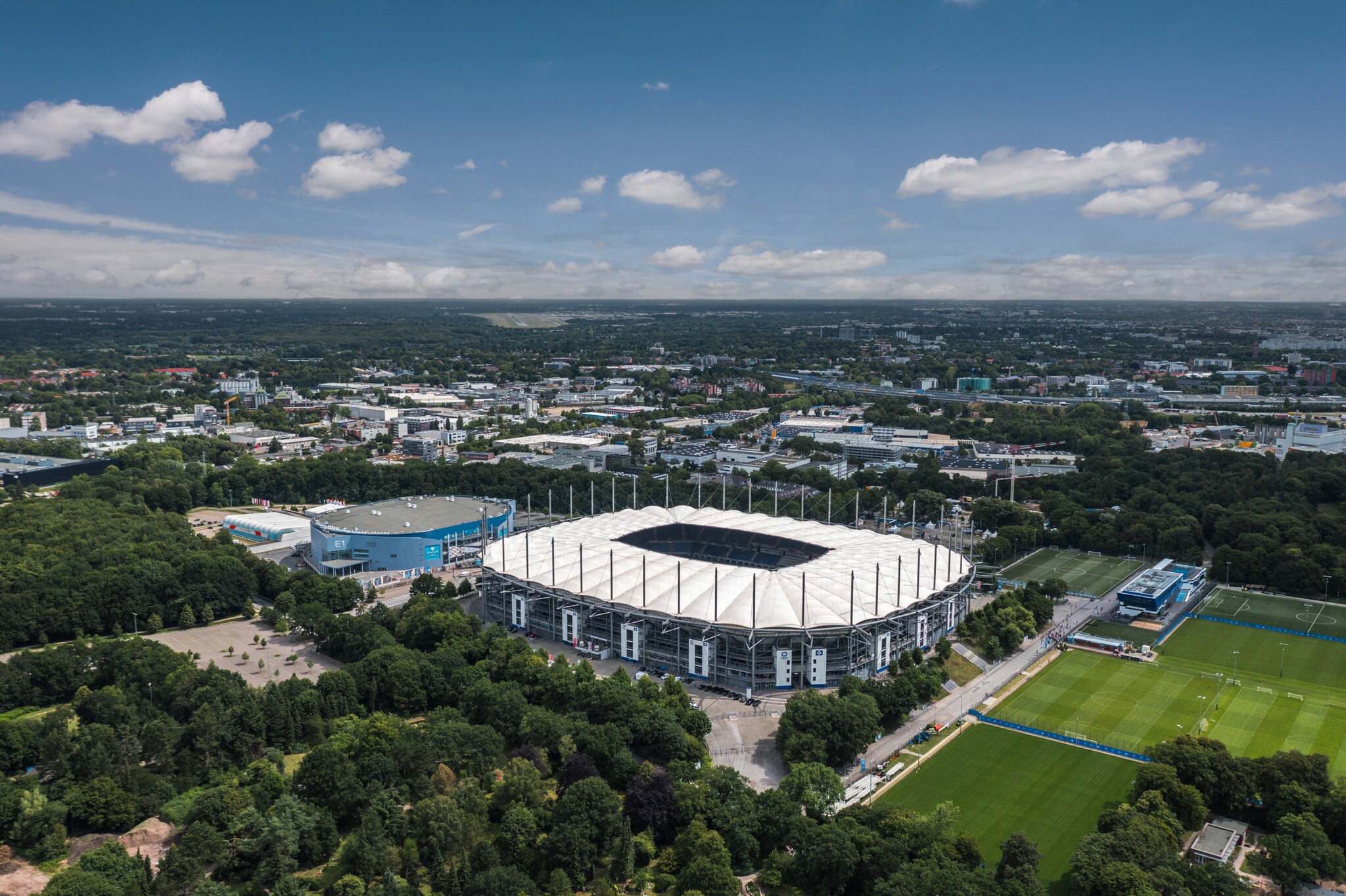 Fußballstadion mit weißem Dach in Grünanlage im städtischen Großraum von oben. Fußballstadion mit weißem Dach in Grünanlage im städtischen Großraum von oben.
