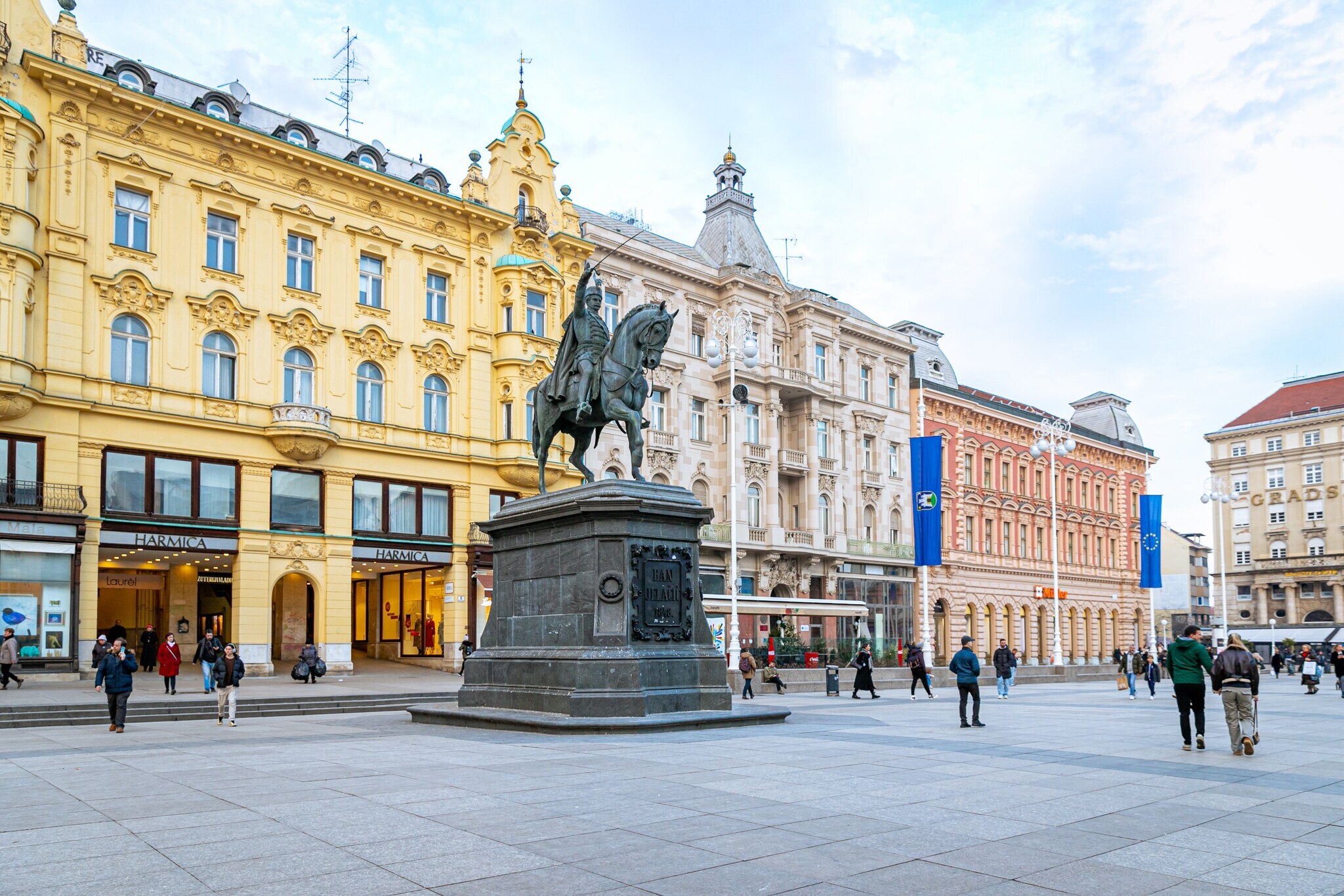 Personen auf einem historischen Platz mit Häusern in unterschiedlichen Architekturstilen und Reiterstandbild.
