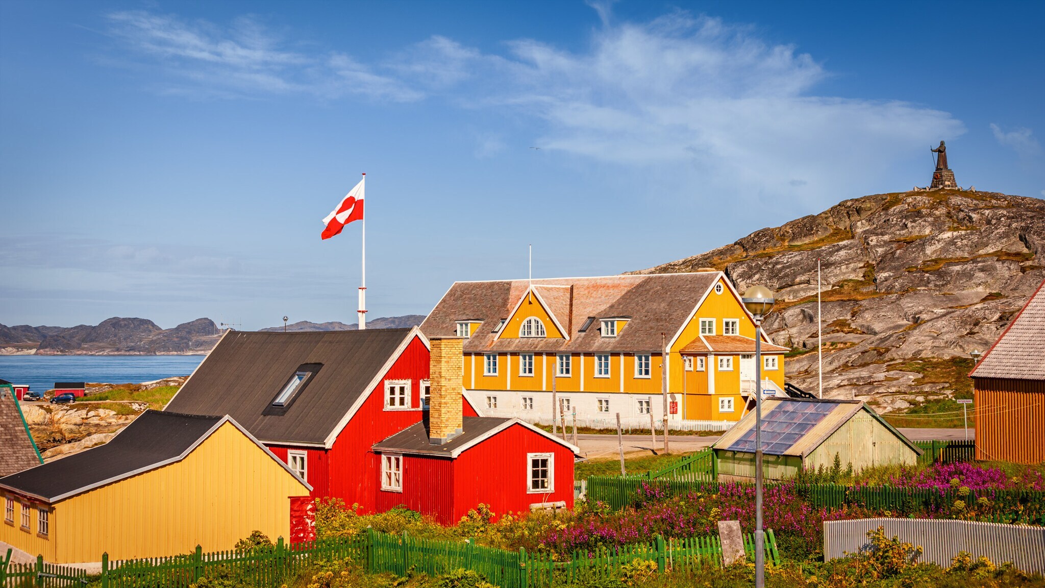 gelbe und rote Gebäude im Bereich des alten Kolonialhafens mit der Hans-Egede-Statue im Hintergrund. gelbe und rote Gebäude im Bereich des alten Kolonialhafens mit der Hans-Egede-Statue im Hintergrund.
