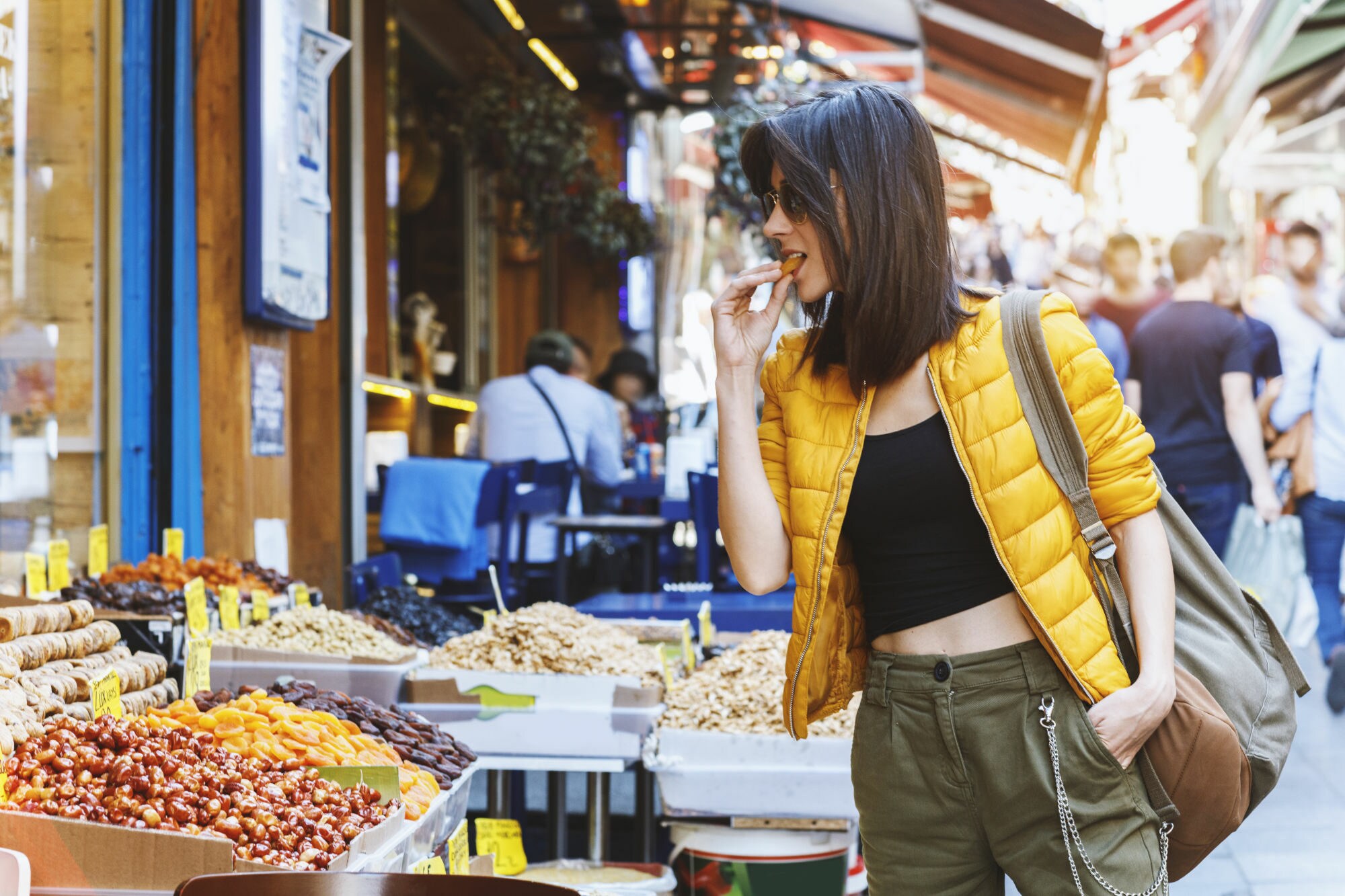 Eine Frau mit Sonnenbrille probiert eine Dattel von einem Marktstand in einer Einkaufsstraße. Eine Frau mit Sonnenbrille probiert eine Dattel von einem Marktstand in einer Einkaufsstraße.