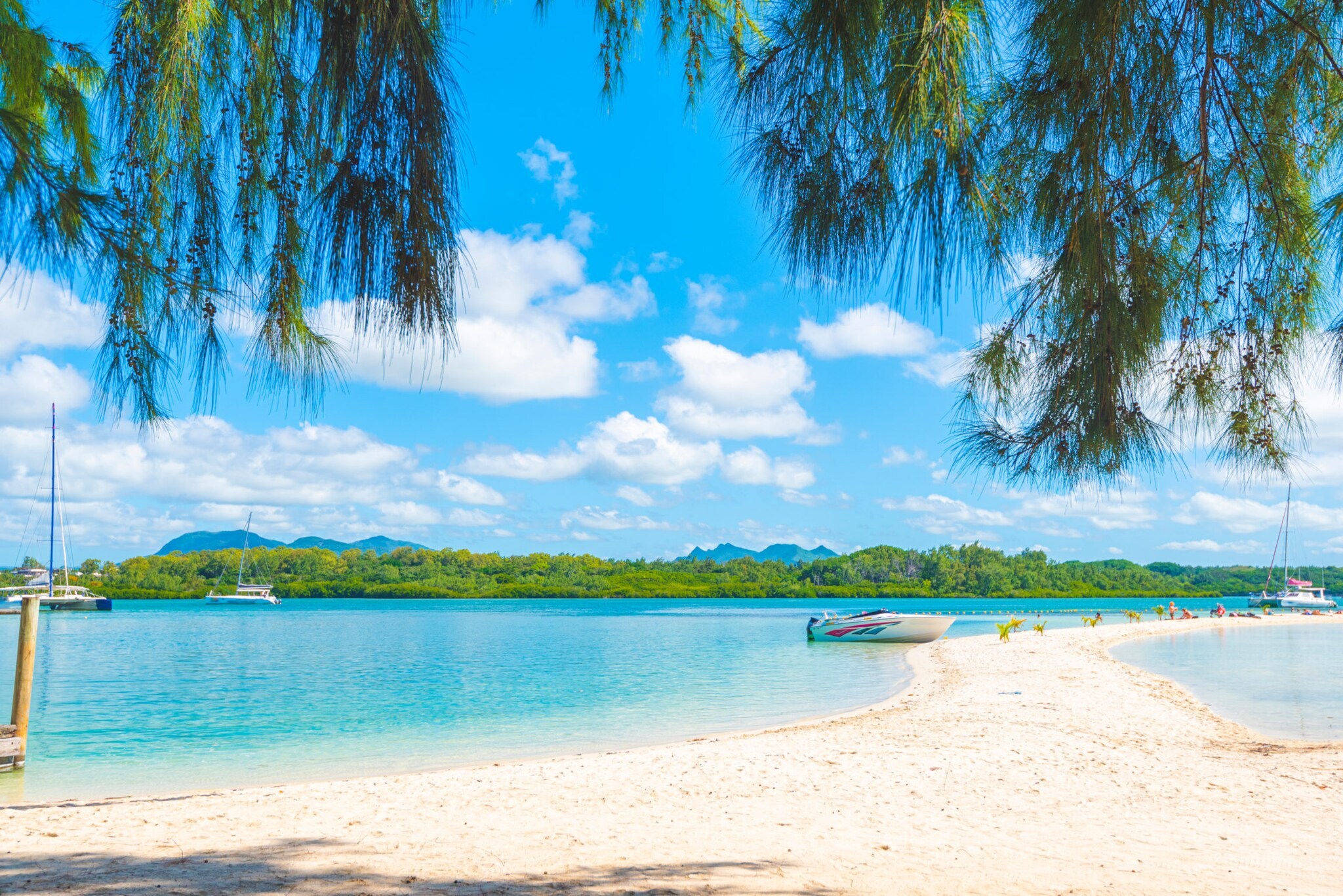 Ein Motorboot an einer weißen Sandbank, umgeben von türkisblauem Meer, im Hintergrund eine Insel mit tropischer Vegetation.