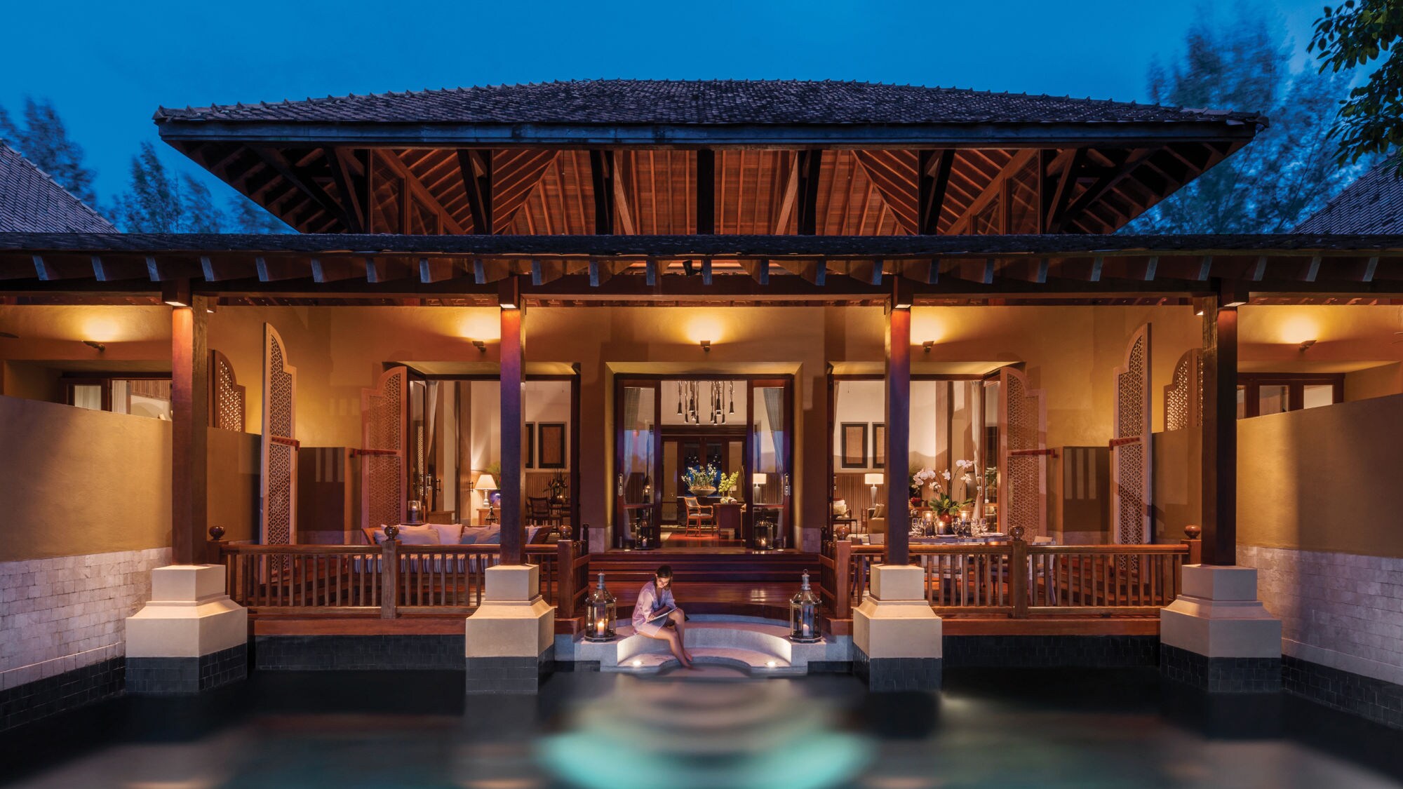 Villa mit offenem Wohnbereich und beleuchtetem Pool, eine Person sitzt am Poolrand, Abendstimmung auf Langkawi Four Seasons. Villa mit offenem Wohnbereich und beleuchtetem Pool, eine Person sitzt am Poolrand, Abendstimmung auf Langkawi Four Seasons.