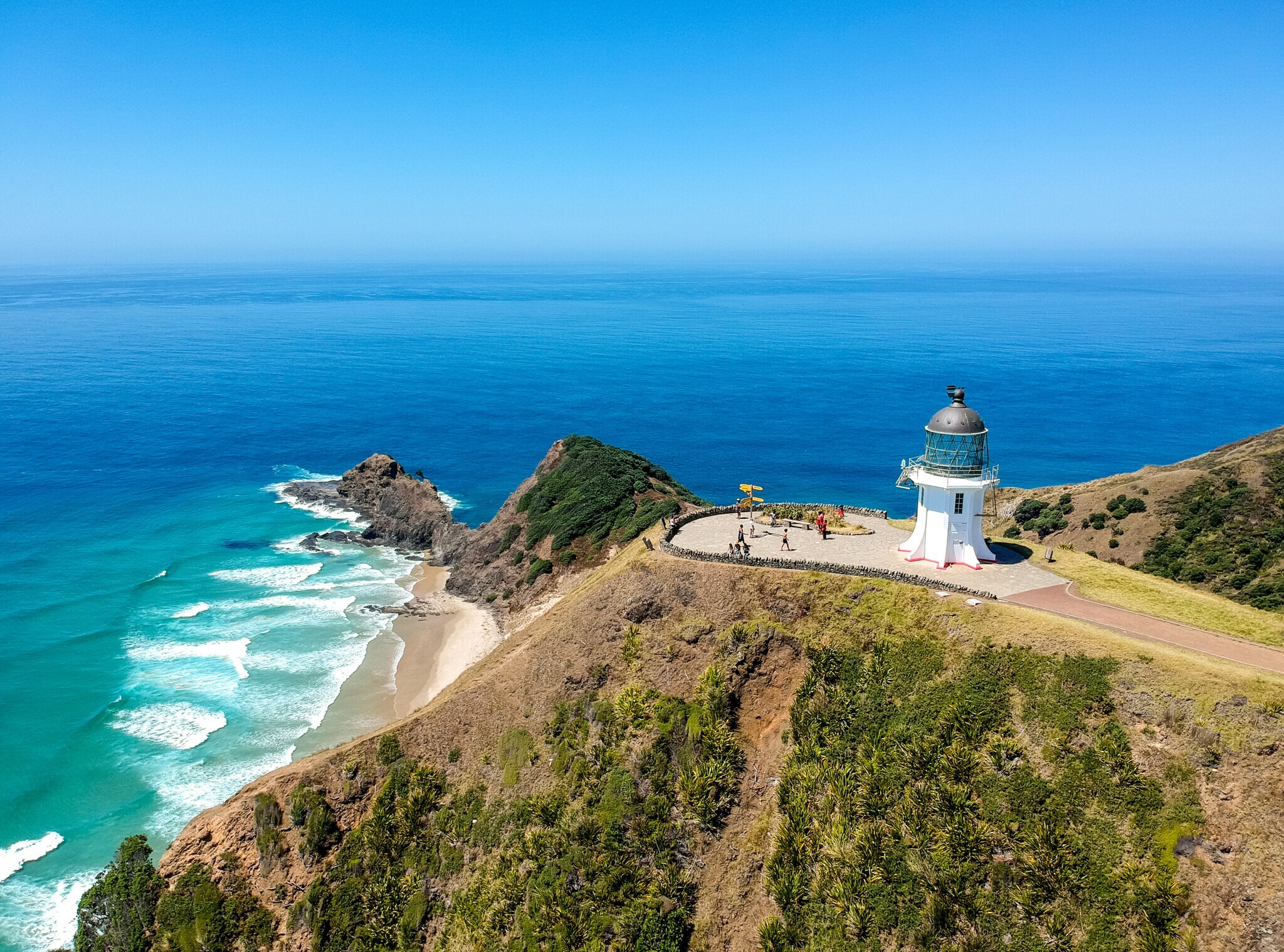 Blick von oben auf einen kleinen Leuchtturm, der nahe einer Klippe steht