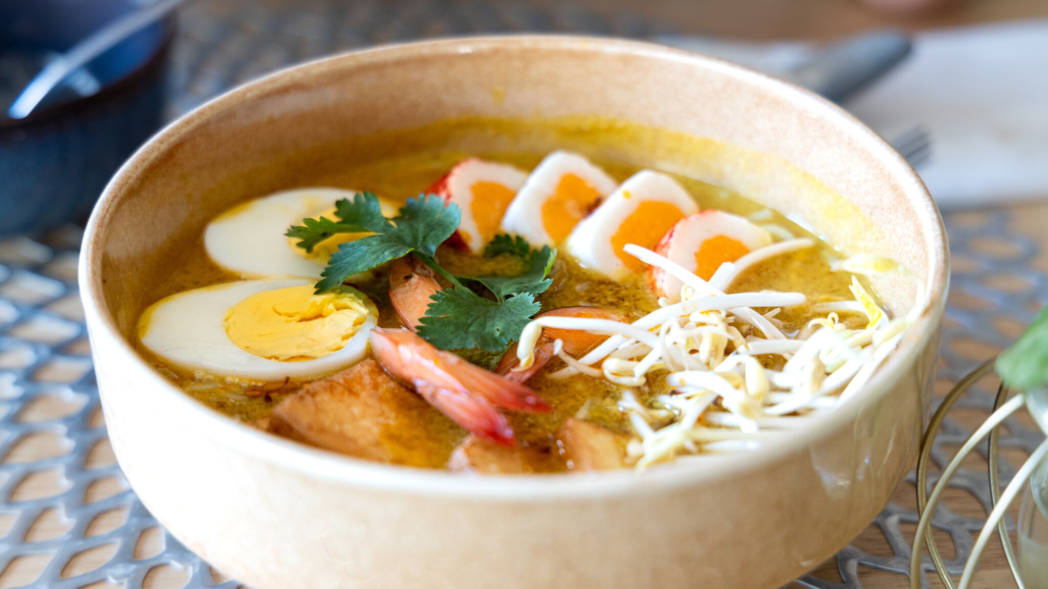 Schale mit Suppe, garniert mit gekochten Eihälften, Garnelen, Sprossen und Korianderblättern.