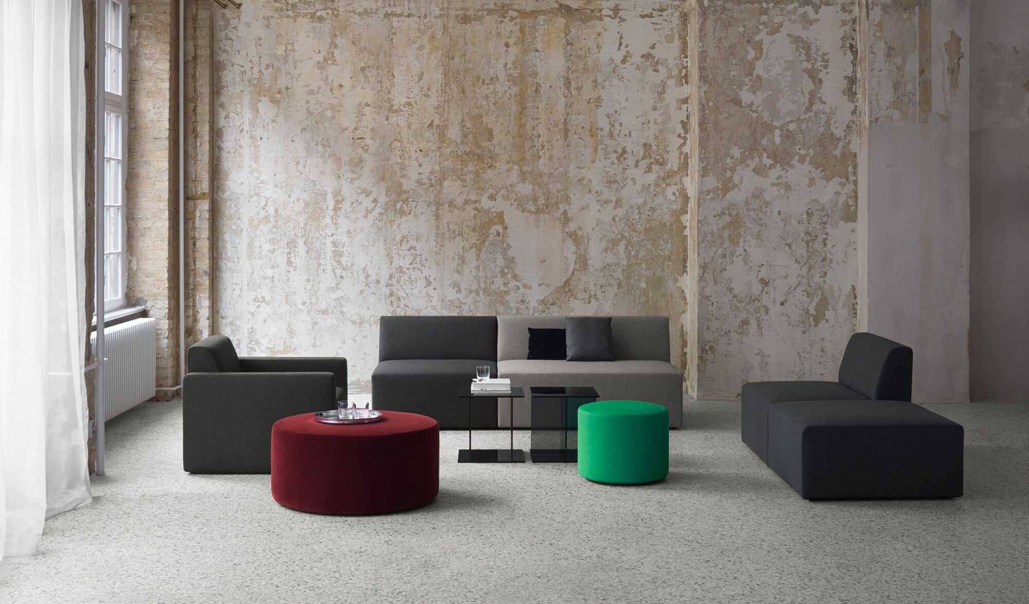 Sitzgruppe aus minimalistischen Polstermöbeln und Beistelltischen in einem großen Raum vor Betonwand Sitzgruppe aus minimalistischen Polstermöbeln und Beistelltischen in einem großen Raum vor Betonwand