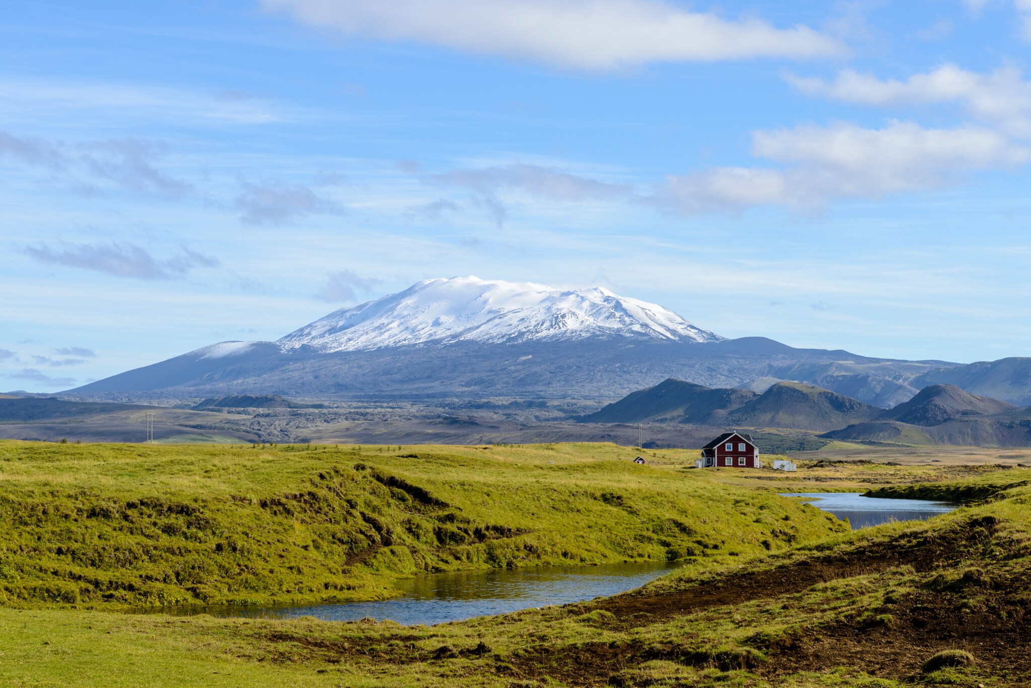 Einsames Haus in weitläufiger grüner Landschaft, mit dem schneebedeckten Vulkan Hekla im Hintergrund. Einsames Haus in weitläufiger grüner Landschaft, mit dem schneebedeckten Vulkan Hekla im Hintergrund.