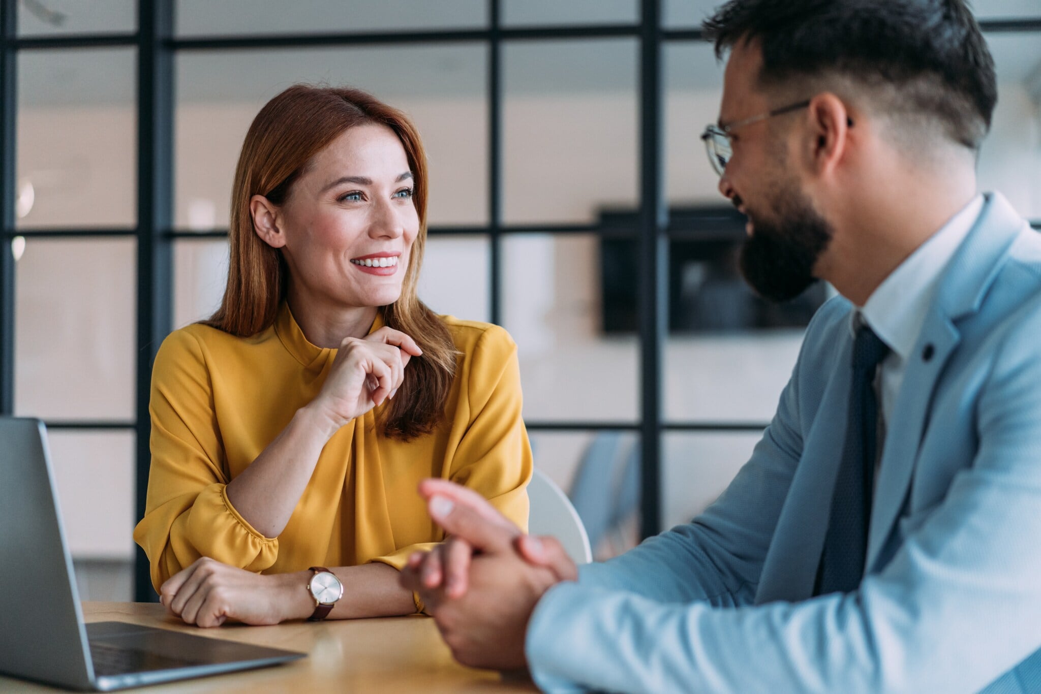 Eine Frau und ein Mann in eleganter Kleidung führen ein freundliches Gespräch an einem Tisch in einem Büro. Eine Frau und ein Mann in eleganter Kleidung führen ein freundliches Gespräch an einem Tisch in einem Büro.