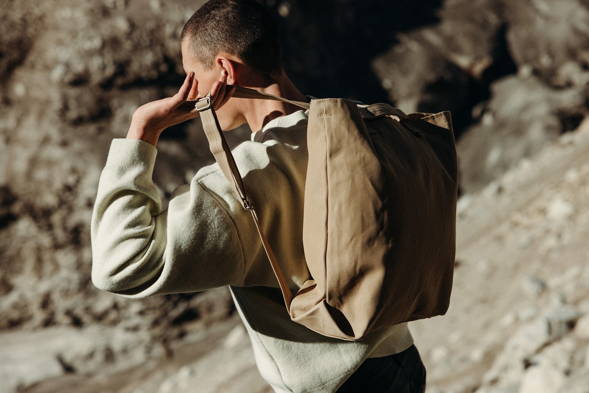 Ein männliches Model trägt in steiniger Umgebung einen Rucksack.