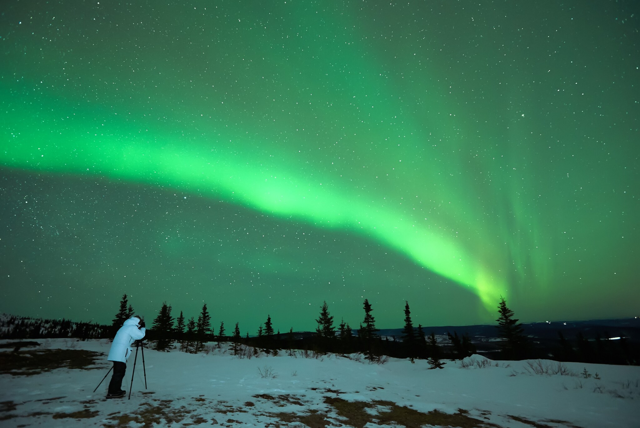 Eine Person fotografiert grüne Polarlichter in einer Winterlandschaft. Eine Person fotografiert grüne Polarlichter in einer Winterlandschaft.