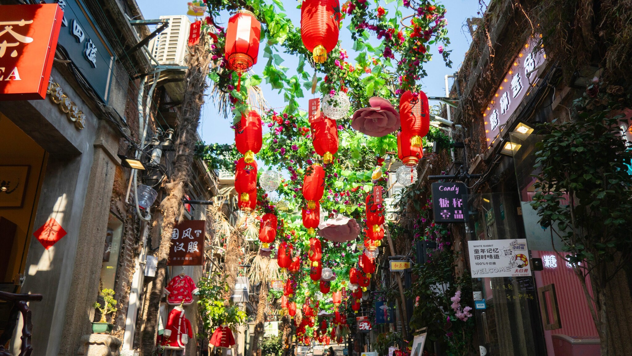 Mit Ranken, Kunstblumen und roten Lampions überhangene Gasse mit Geschäften. Mit Ranken, Kunstblumen und roten Lampions überhangene Gasse mit Geschäften.