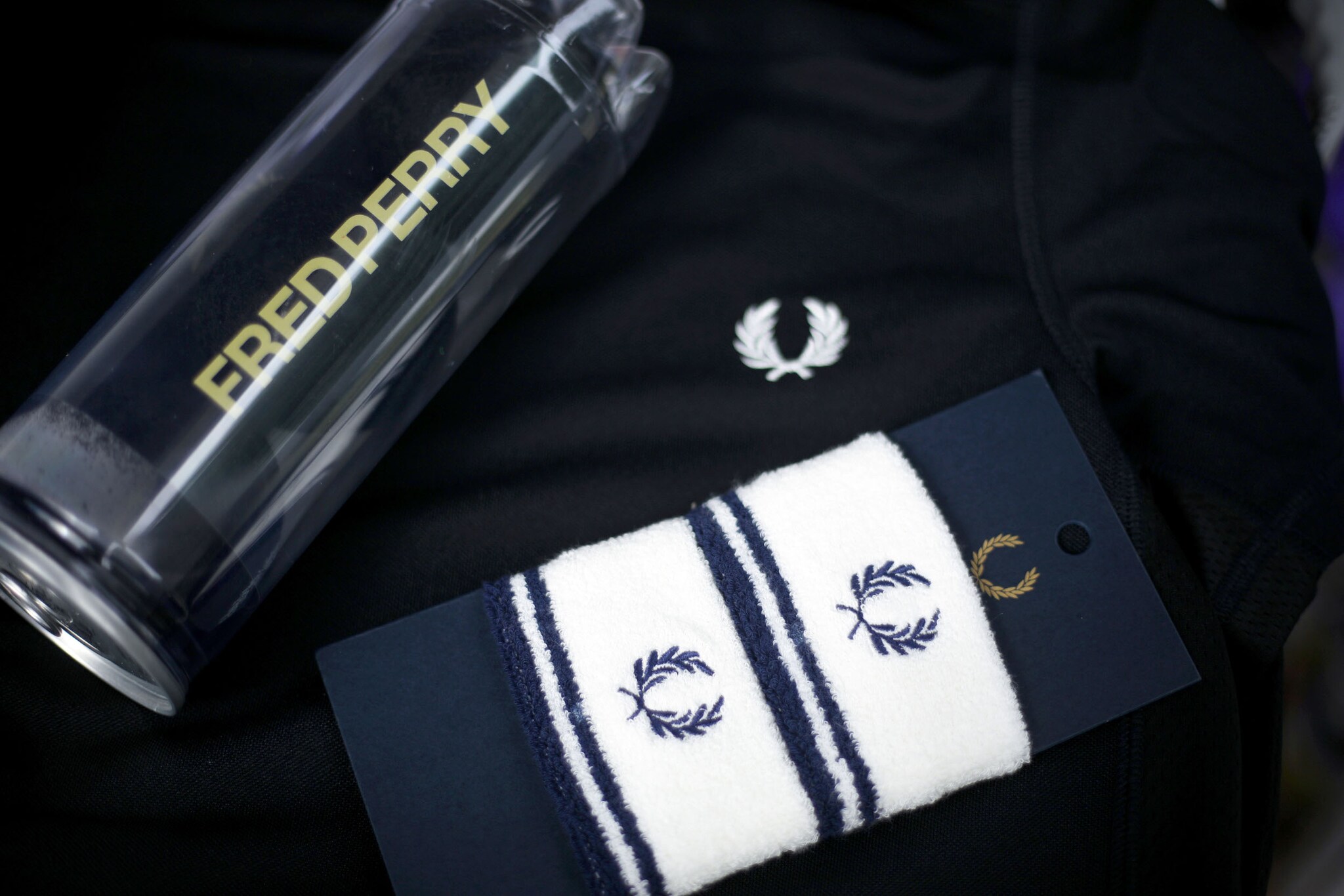 Zwei Schweißbänder und eine Wasserflasche auf einem Sweatshirt der Marke Fred Perry mit Lorbeerkranz-Logo