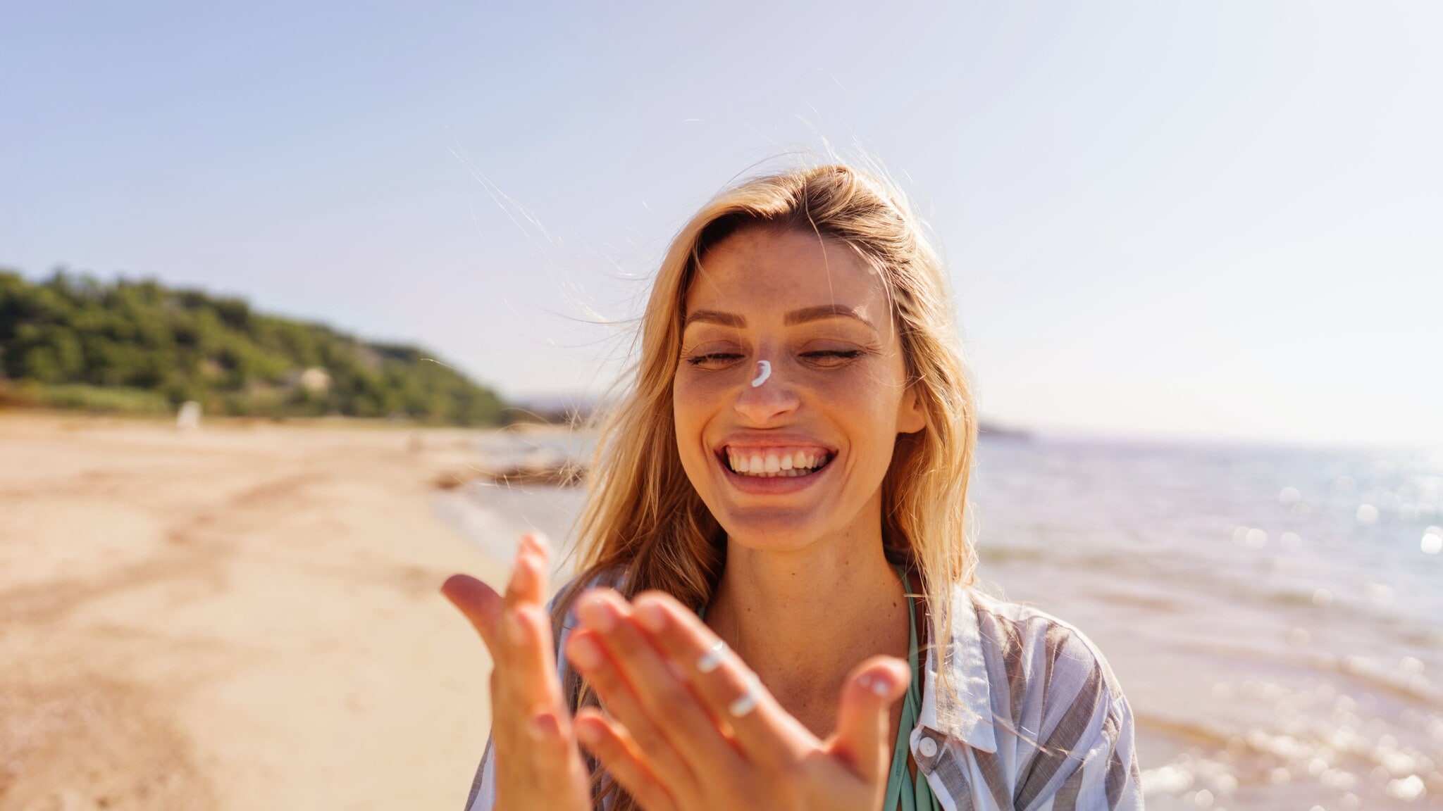 Eine lachende Frau mit Sonnencreme auf Händen und Gesicht an einem Strand. Eine lachende Frau mit Sonnencreme auf Händen und Gesicht an einem Strand.