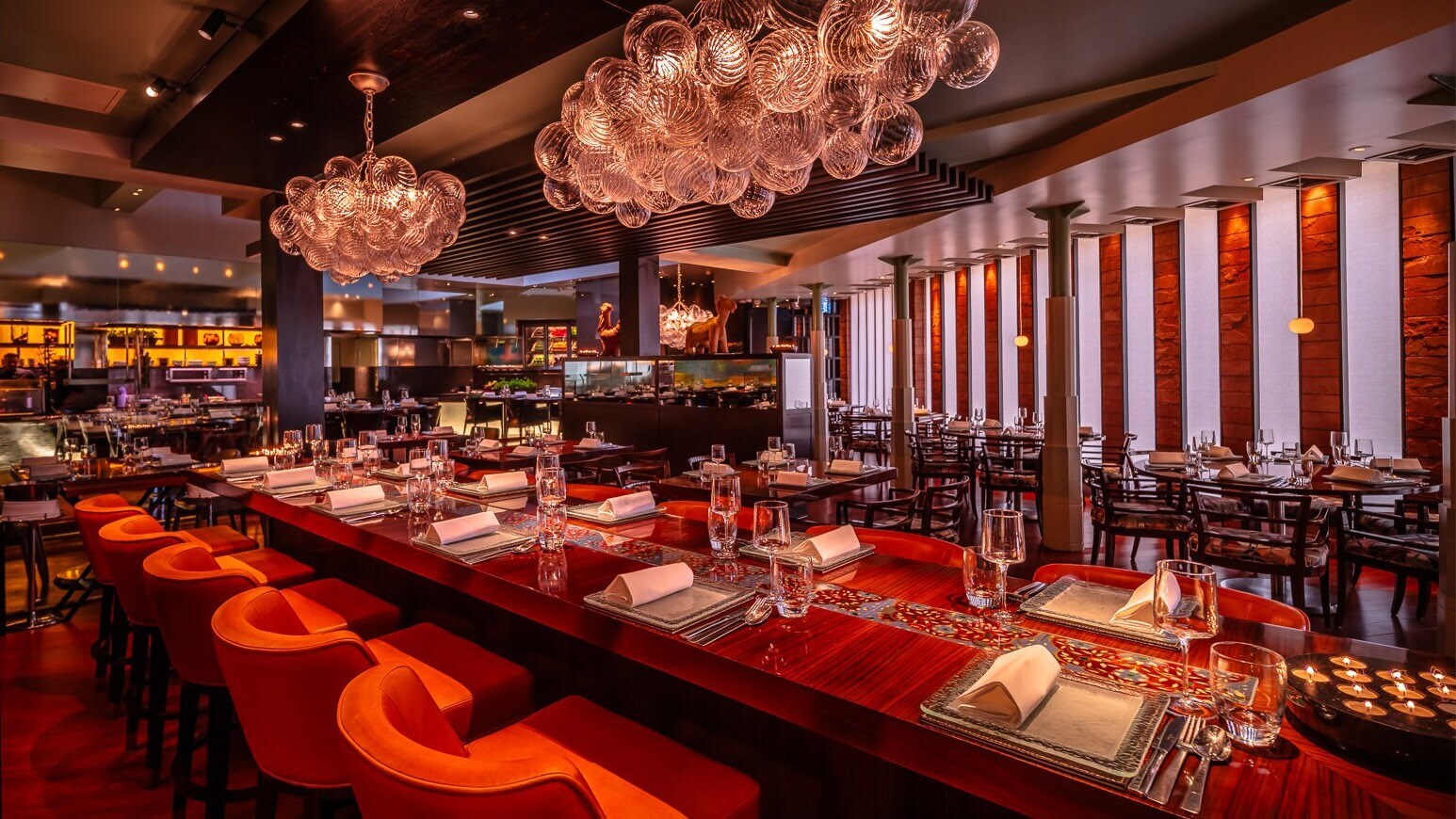 Opulent eingerichteter Speisesaal mit eingedeckter Holztafel und offener Küche.