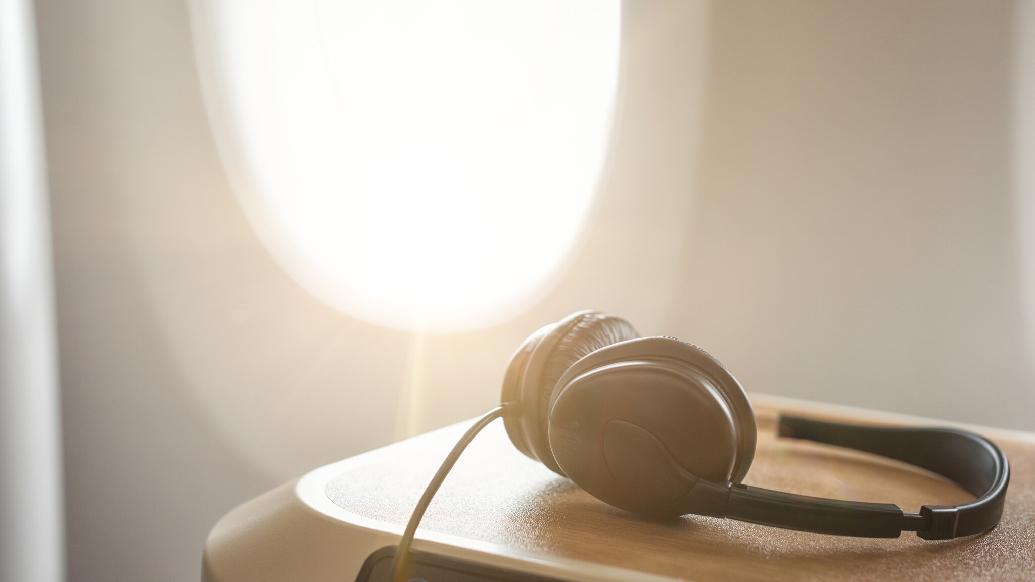 Schwarzer Kopfhörer liegt auf einer braunen Ablage vor einem Fenster im Flugzeug mit Sonnenlicht