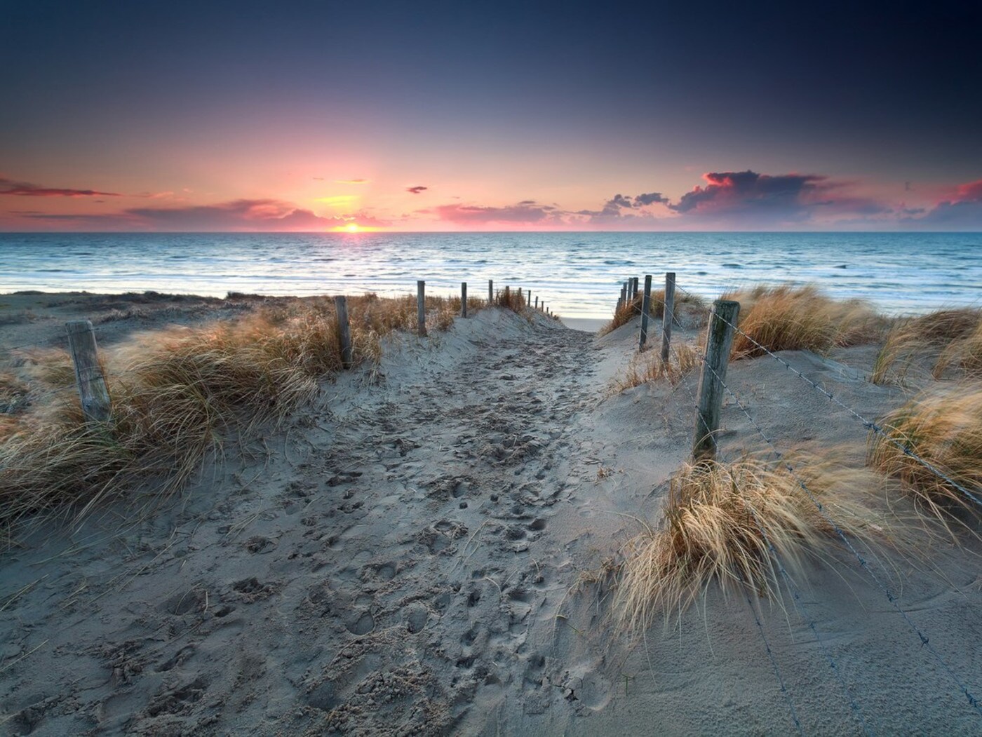 Ein Sandweg mit Dünengras und der untergehenden Sonne über der Ostsee