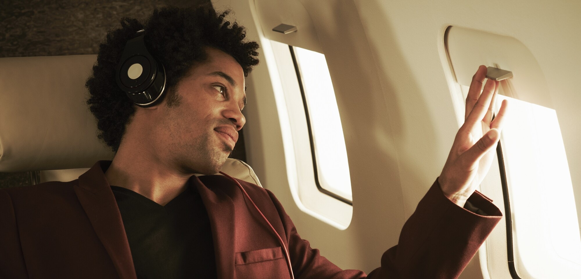 Platz eins auf deiner Packliste: Noise-Cancelling-Kopfhörer Fluggast mir Kopfhörern schaut aus dem Fenster.