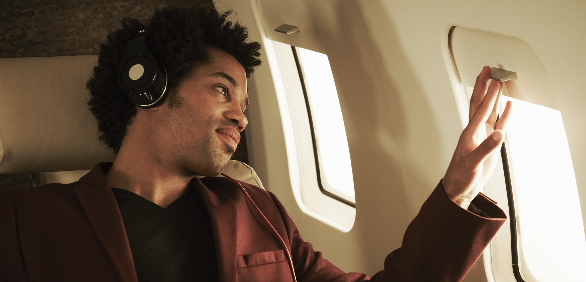 Platz eins auf deiner Packliste: Noise-Cancelling-Kopfhörer Fluggast mir Kopfhörern schaut aus dem Fenster.