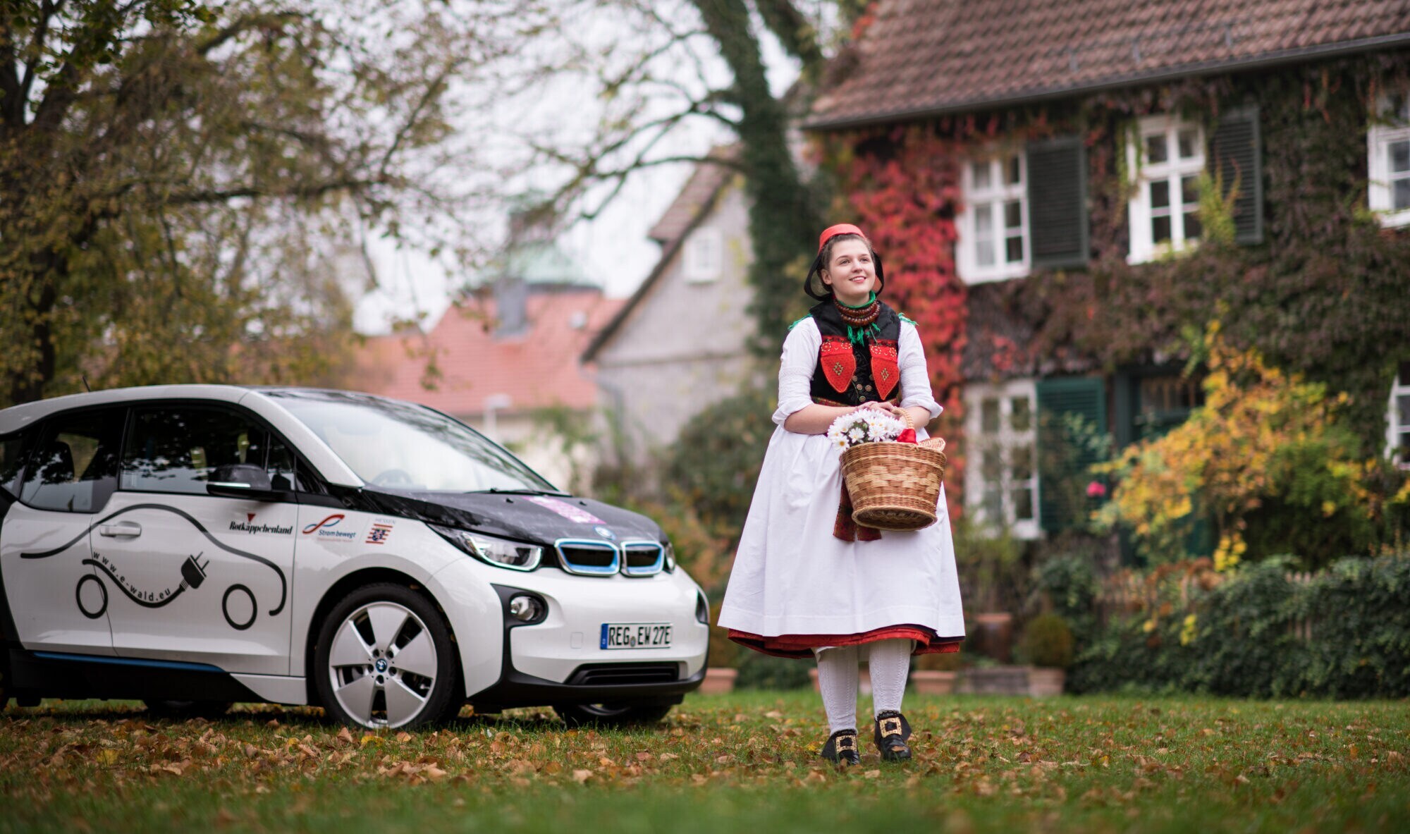 Eine als Rotkäppchen verkleidete Frau neben einem E-Auto