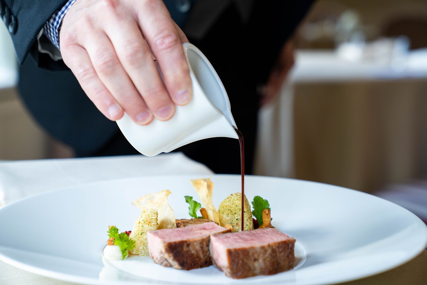 Jemand gießt Sauce über zwei fein angerichtete Stücke Fleisch