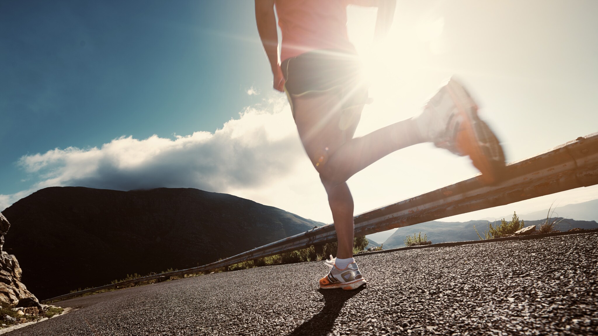 Rückansicht einer Athletin, die eine Straße in den Bergen entlangläuft Rückansicht einer Athletin, die eine Straße in den Bergen entlangläuft