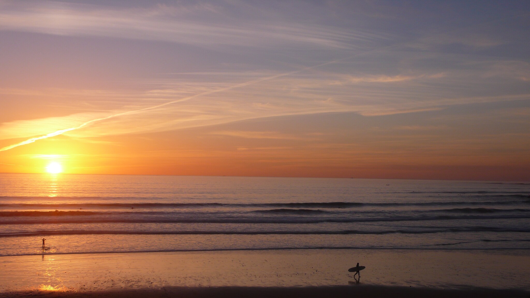 Sandstrand am Meer mit leichten Wellen bei Sonnenuntergang.