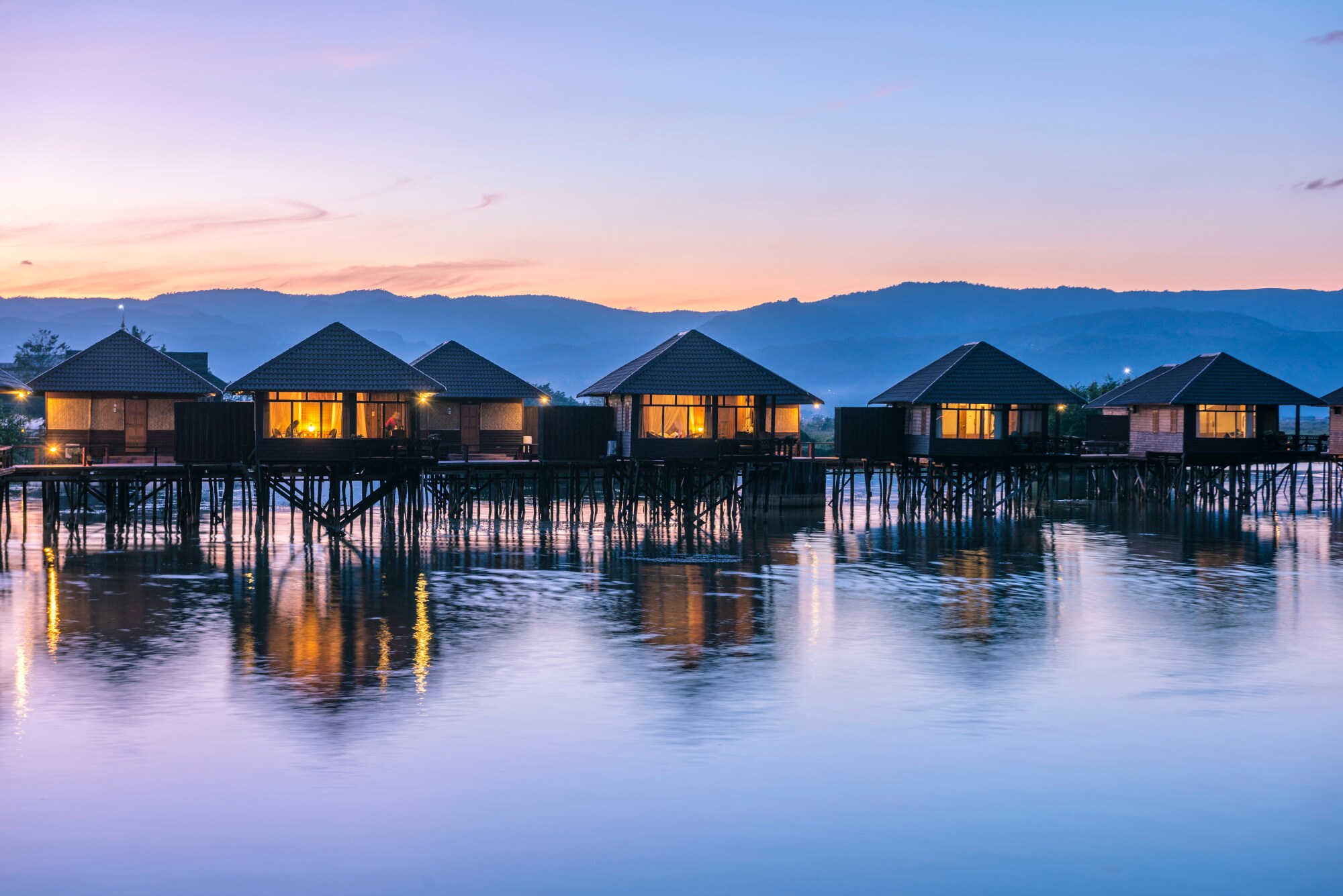 Beleuchtete Bungalows auf Stelzen im Wasser bei Sonnenuntergang Beleuchtete Bungalows auf Stelzen im Wasser bei Sonnenuntergang