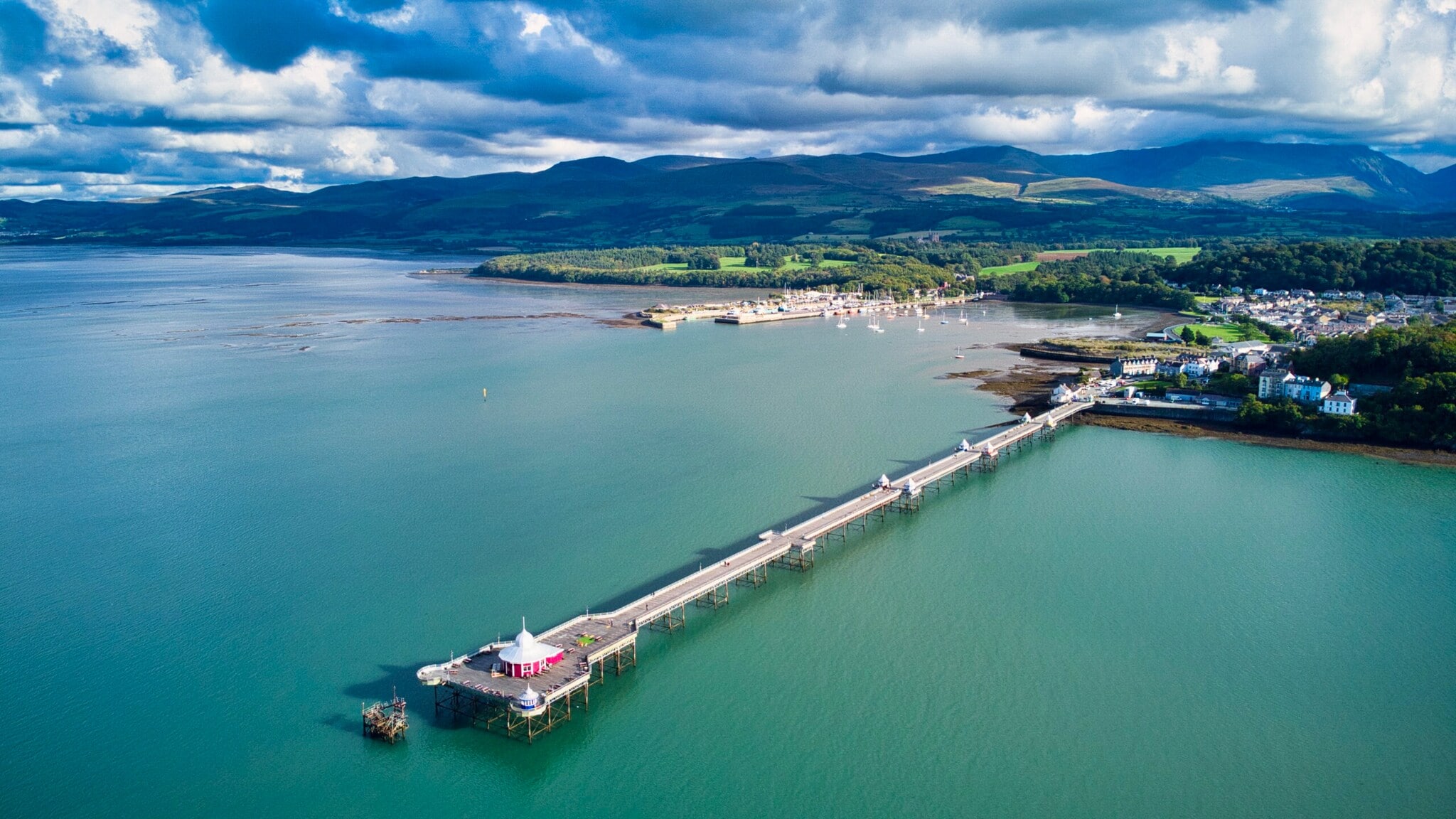 Langer Pier an einem Küstenort, im Hintergrund grüne Hügellandschaft. Langer Pier an einem Küstenort, im Hintergrund grüne Hügellandschaft.