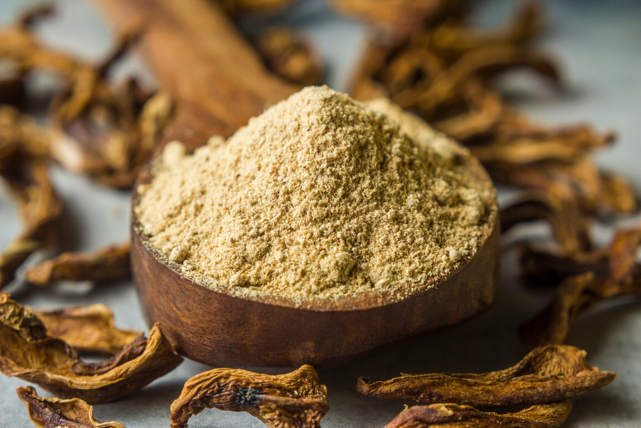Nahaufnahme von trockenem Mangopulver in einer Holzschale umgeben von getrockneten Mangostücken