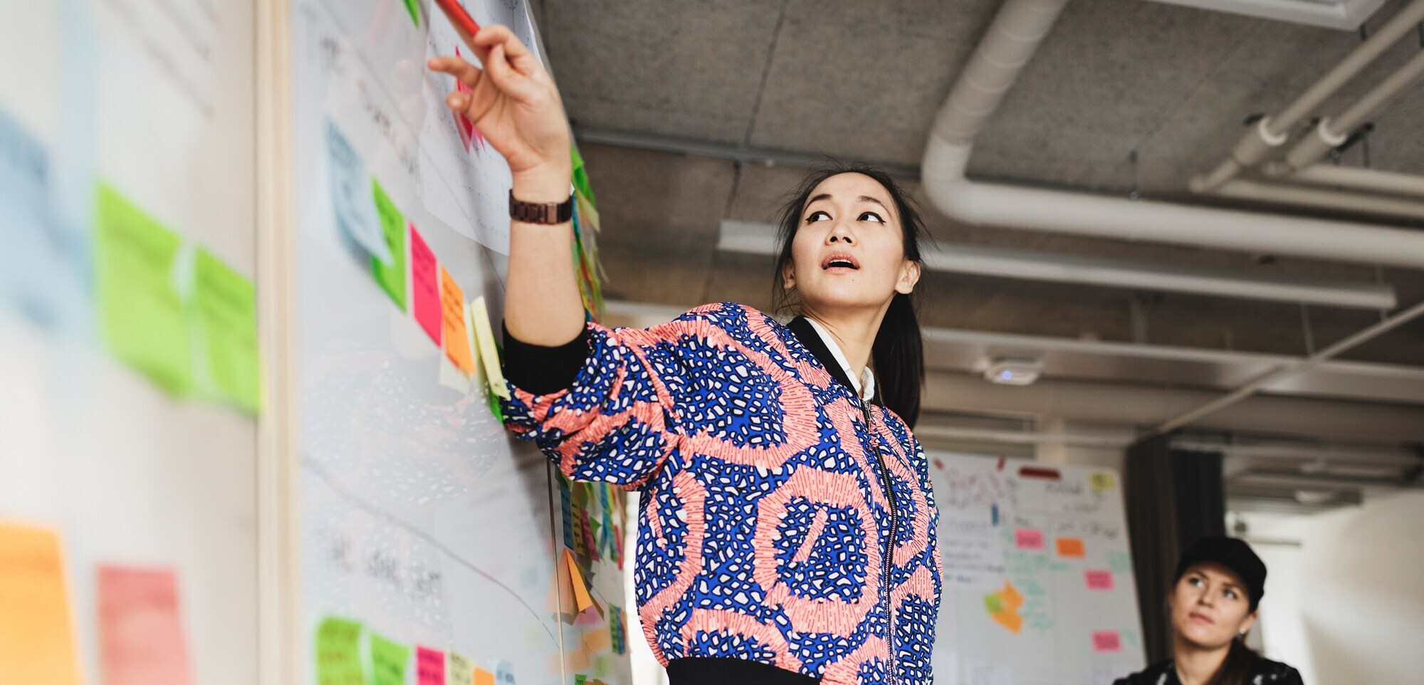 Female Leadership: Echter Mehrwert, nachhaltiger Erfolg Fotografie einer jungen Unternehmerin, die an einem Whiteboard ein Konzept präsentiert.