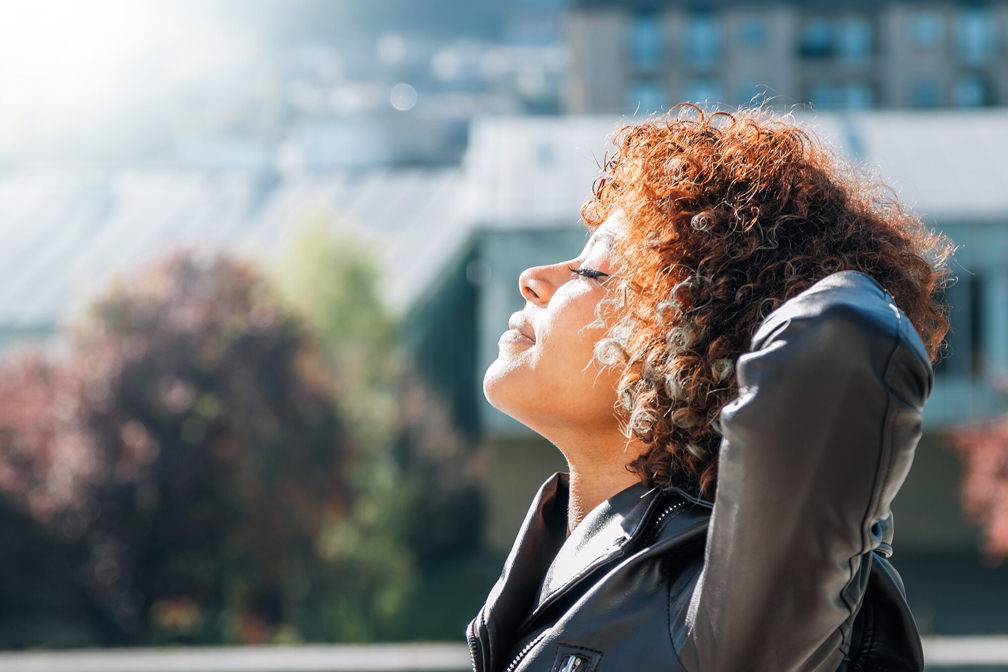 Corporate Scent Eine Frau mit geschlossenen Augen hält ihr Gesicht der Sonne hin. Die Arme hält sie hinter dem Kopf.