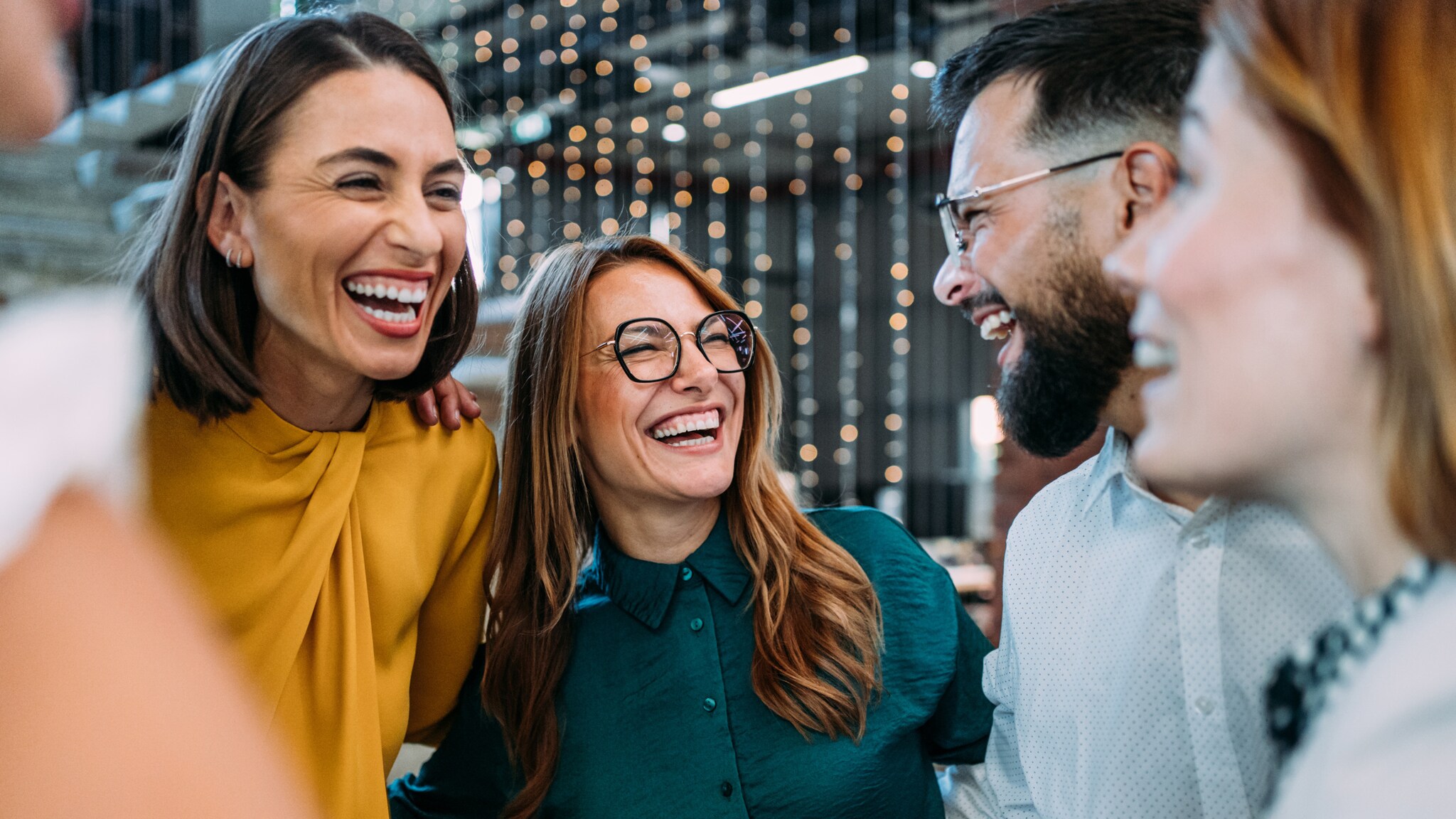 Vier lachende Personen in eleganter Kleidung stehen eng beieinander in einem Büro.