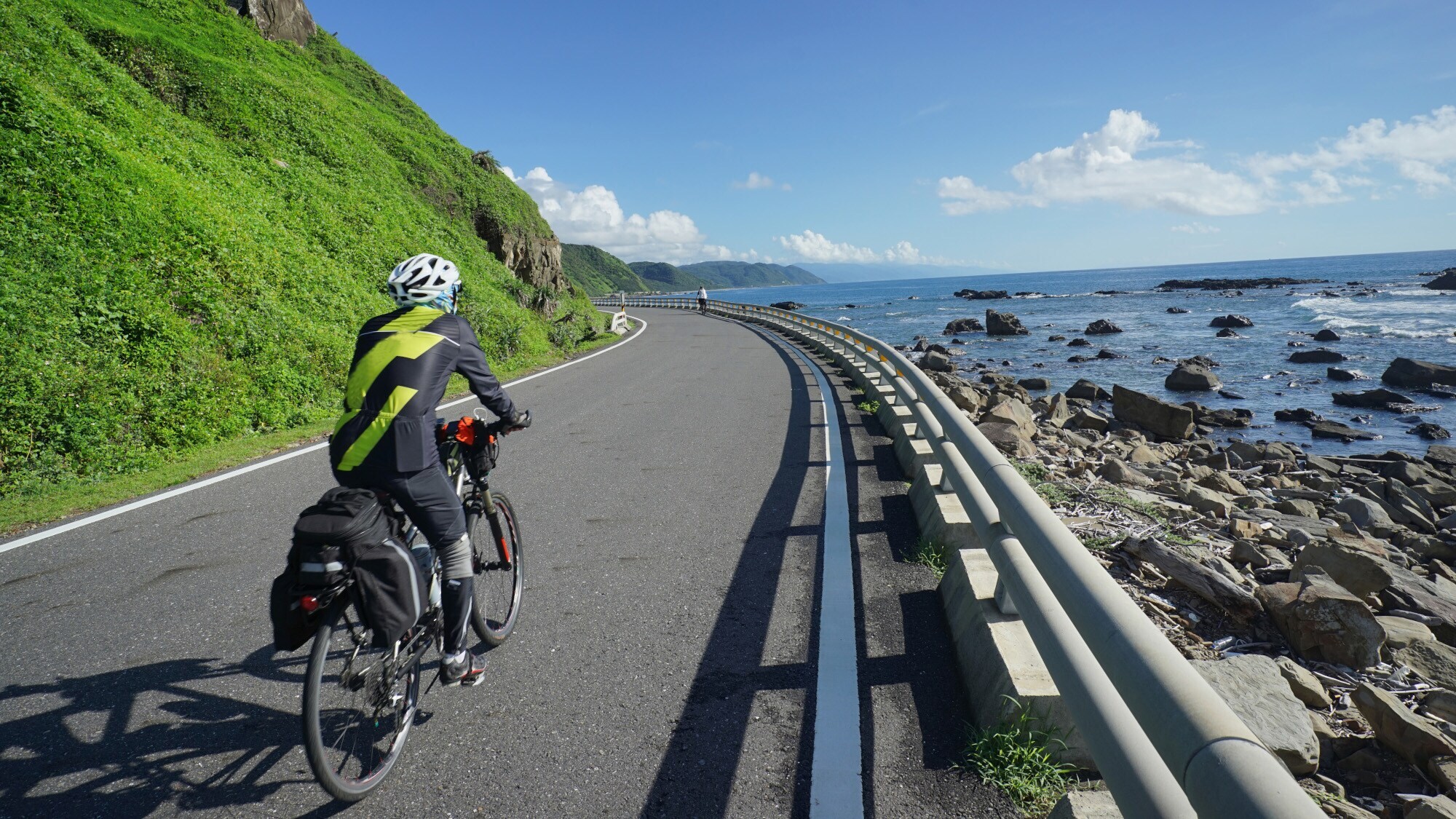 Rückansicht eines fahrenden Mountainbikers auf einer Küstenstraße.