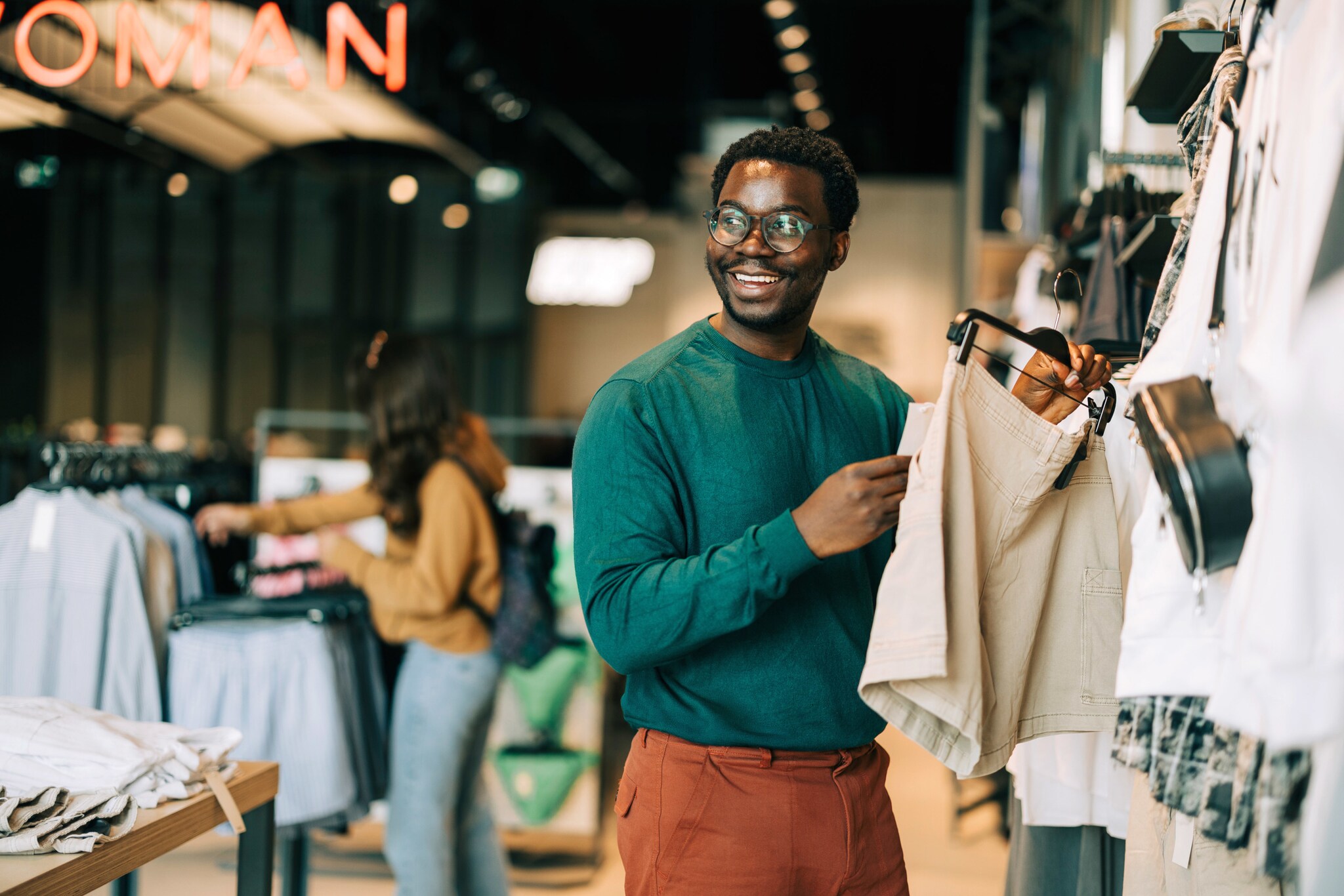 Ein lächelnder Mann hält eine kurze Hose an einem Bügel in seiner Hand in einem Modegeschäft.