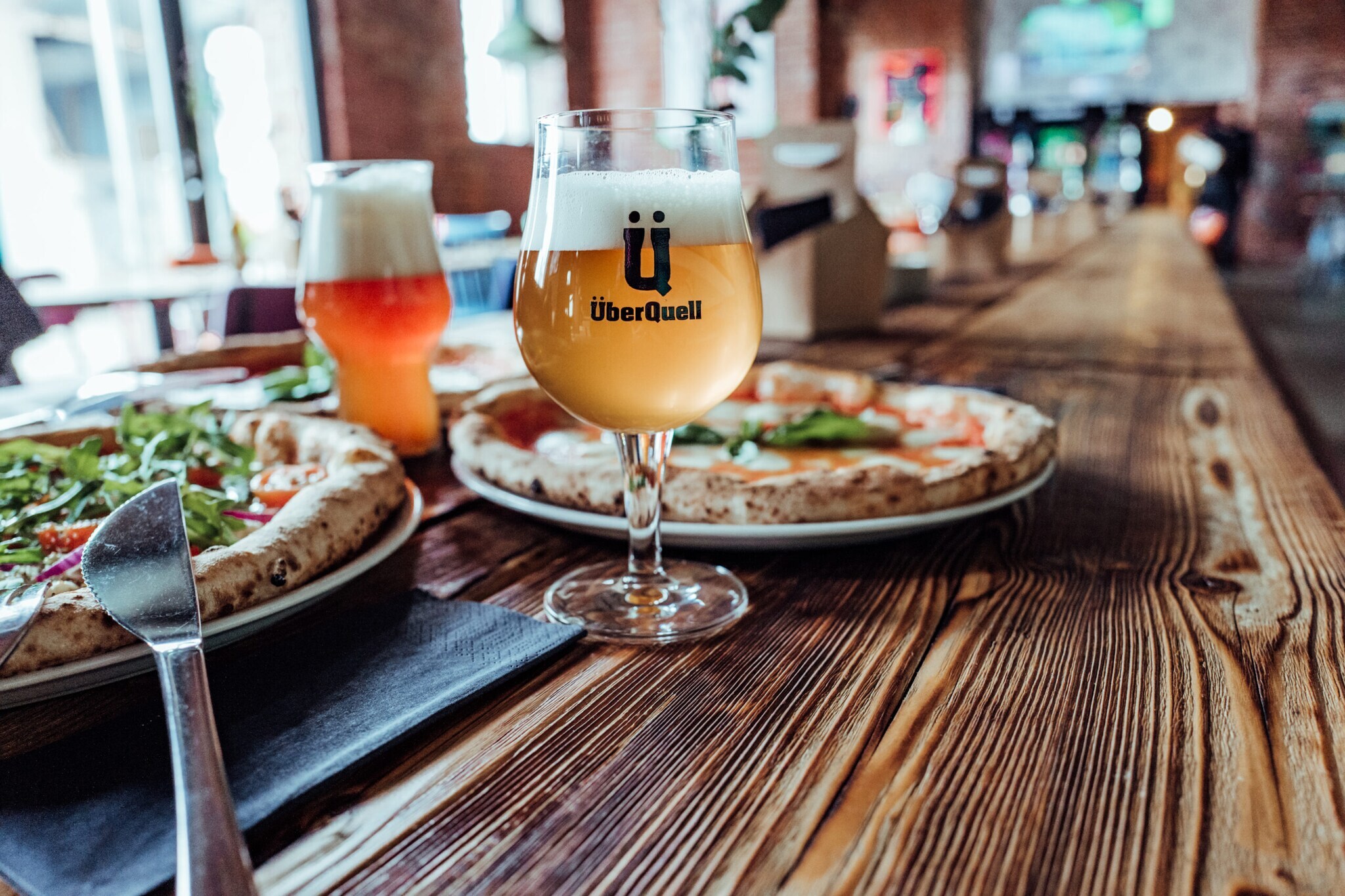 Ein frisch gezapftes Bier steht neben einer Pizza.