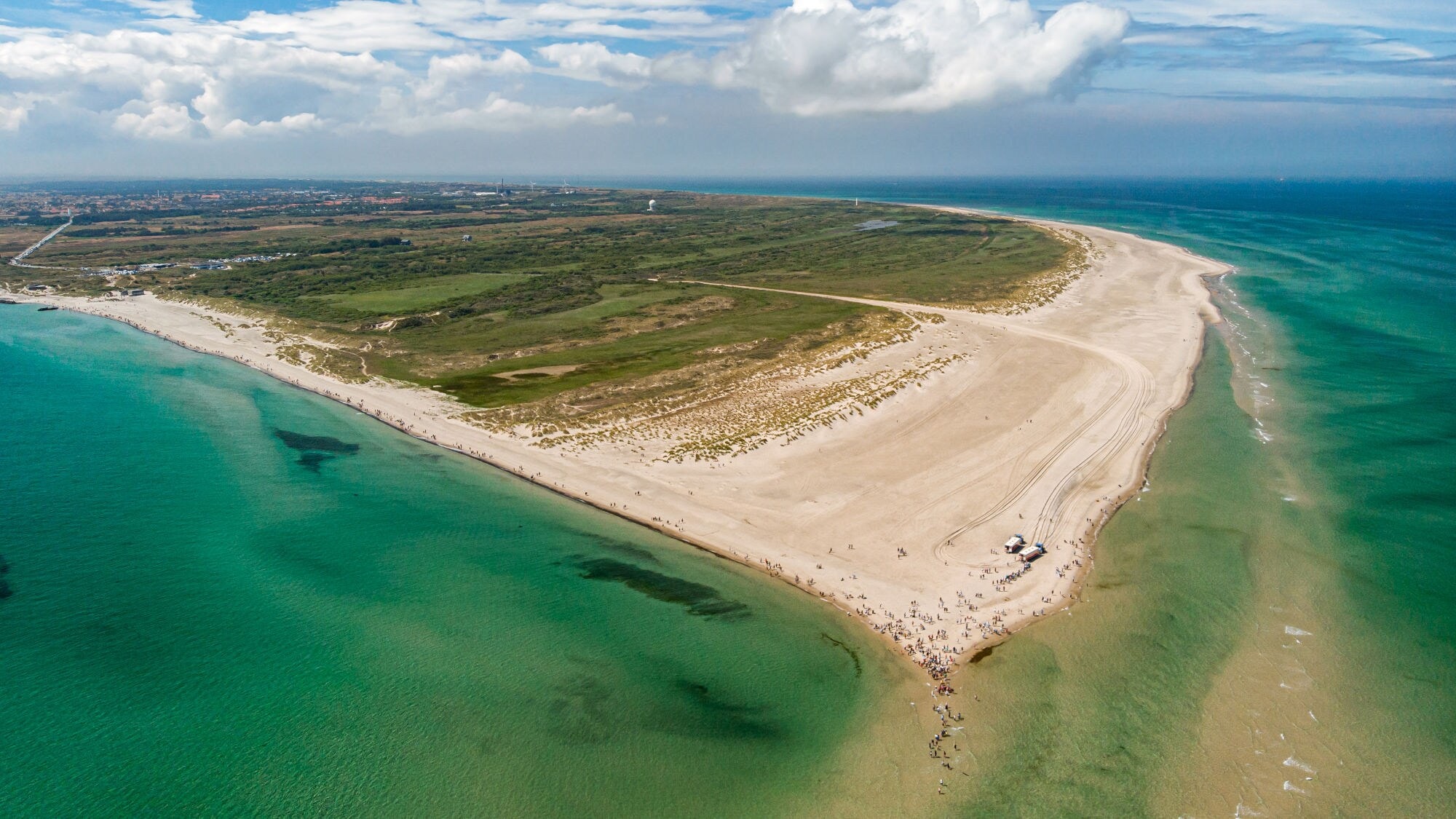 Luftaufnahme einer schmalen Landzunge mit Sandstrand und grüner Vegetation, umgeben von blauem Meer unter bewölktem Himmel. Luftaufnahme einer schmalen Landzunge mit Sandstrand und grüner Vegetation, umgeben von blauem Meer unter bewölktem Himmel.