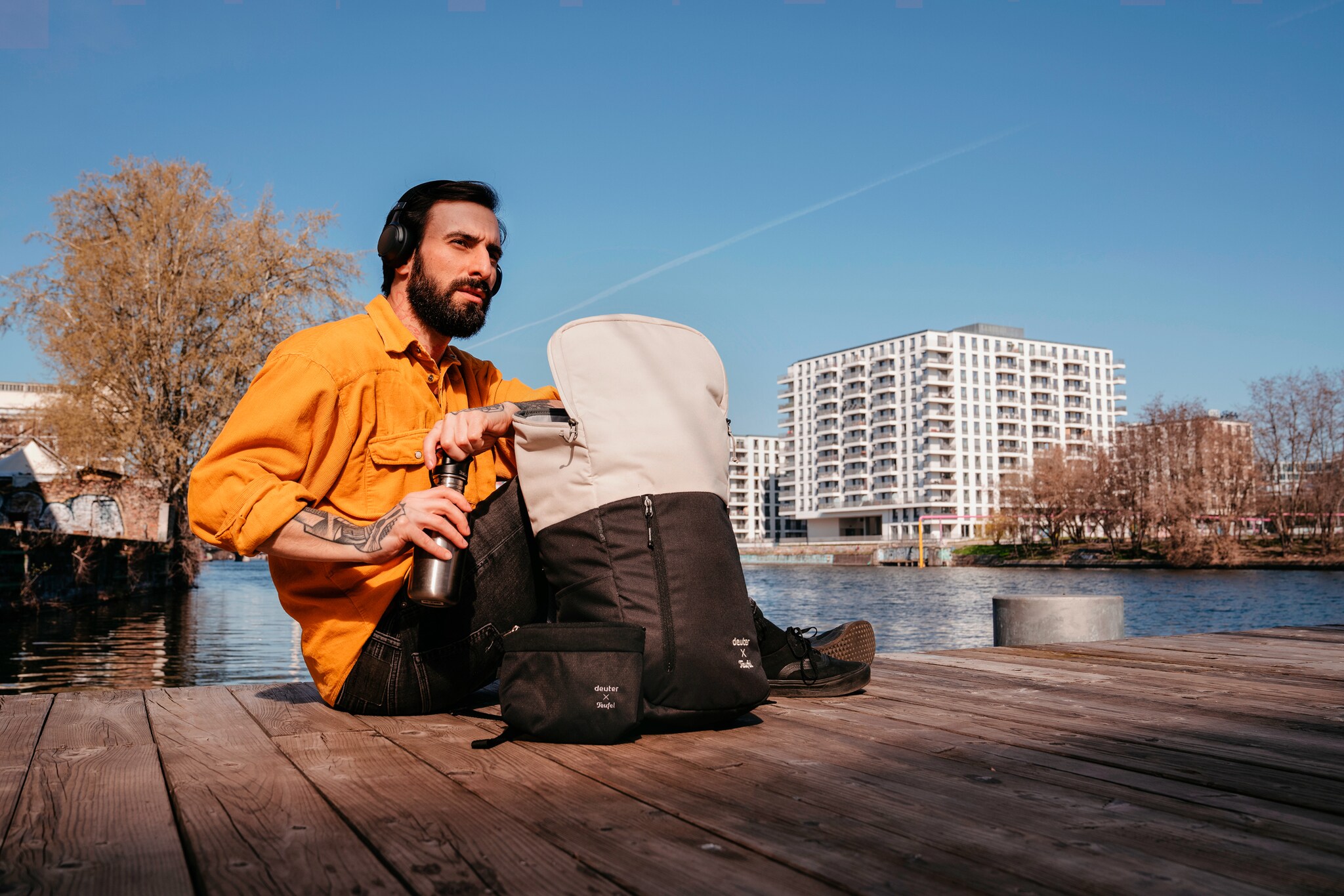 Ein am Wasser sitzender Mann mit geöffnetem Rucksack neben sich