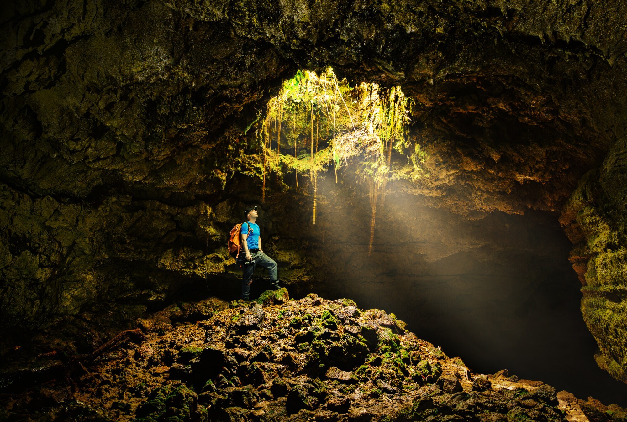 Ein Mann in einer Felshöhle schaut durch ein Loch über ihm ins Licht.