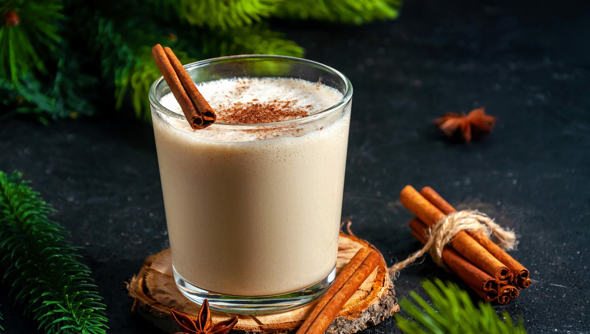 Eggnogg im Glas, dekoriert mit Zimtstangen, Tannenzapfen und Anissternen