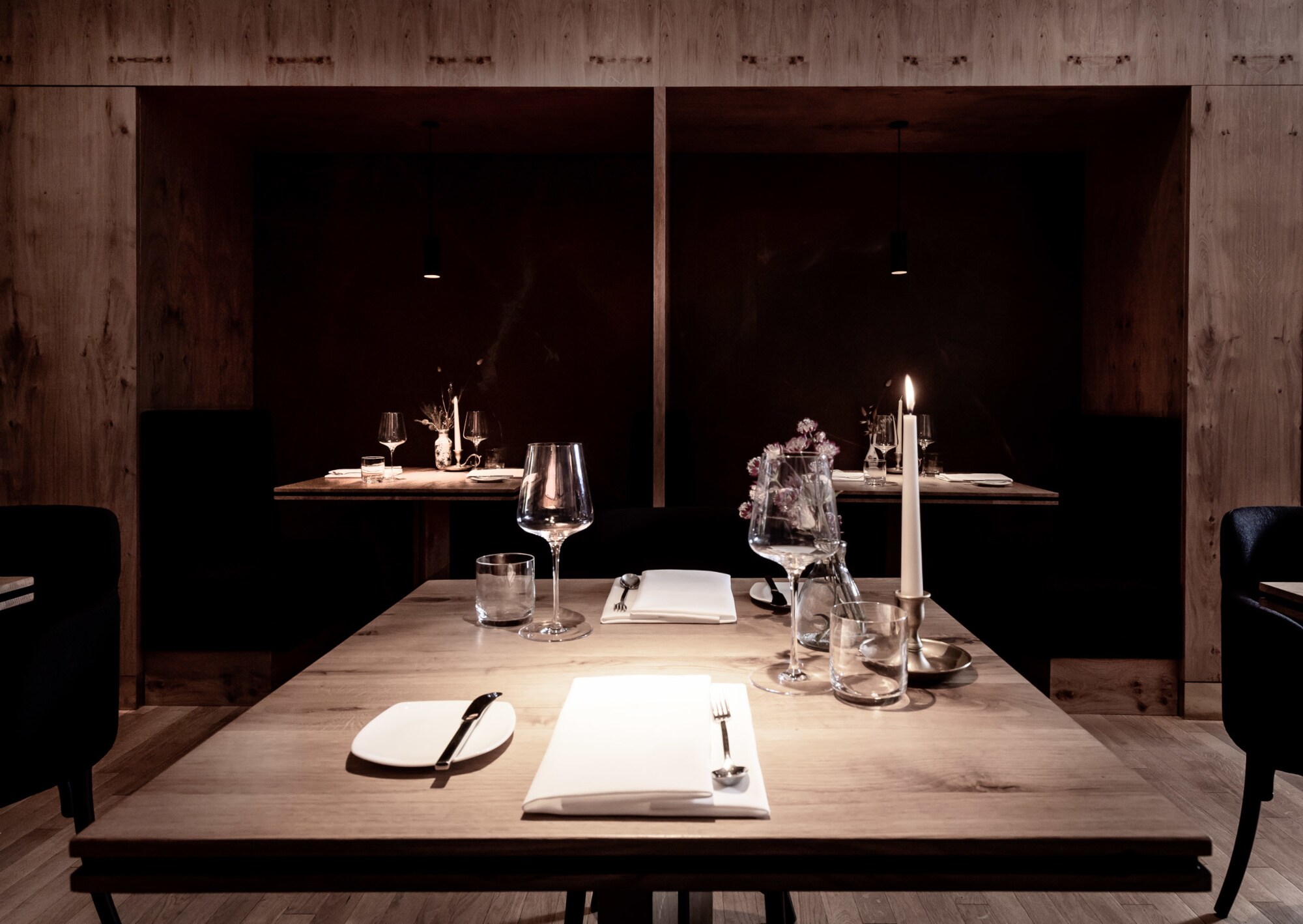 Ein schlicht gedeckter Holztisch für zwei Personen mit brennender Kerze.
