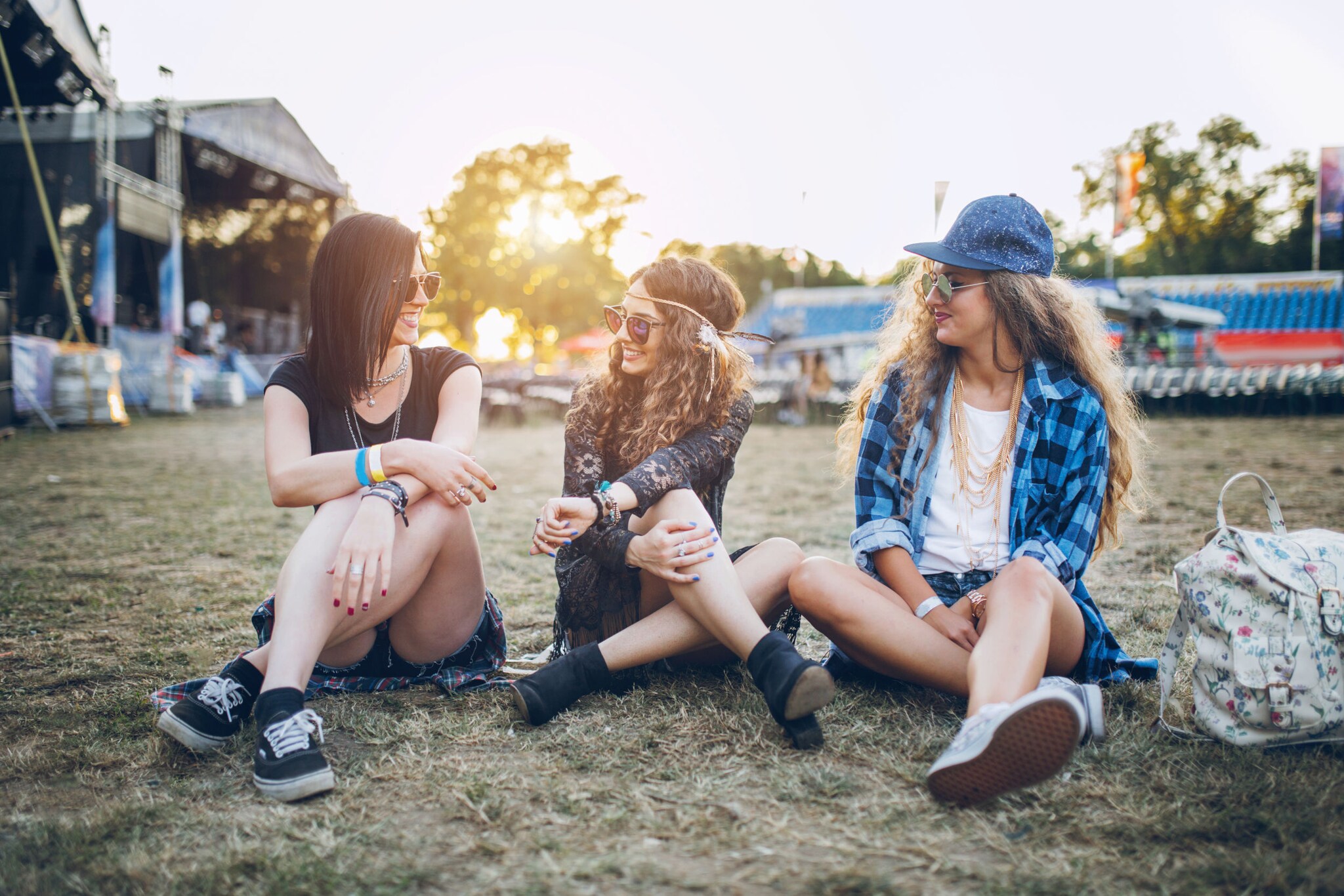 Drei Frauen sitzen auf einem Festivalgelände, hinter ihnen die Bühne.