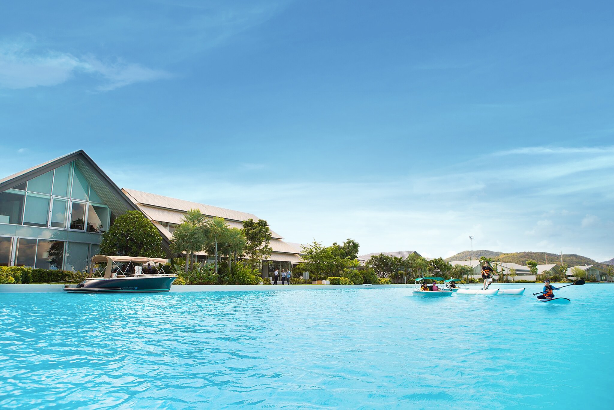 Ein klarer, meeresartiger Pool mit Thailand-typischen Booten vor dem Hintergrund luxuriöser Villen und Hügel Ein klarer, meeresartiger Pool mit Thailand-typischen Booten vor dem Hintergrund luxuriöser Villen und Hügel