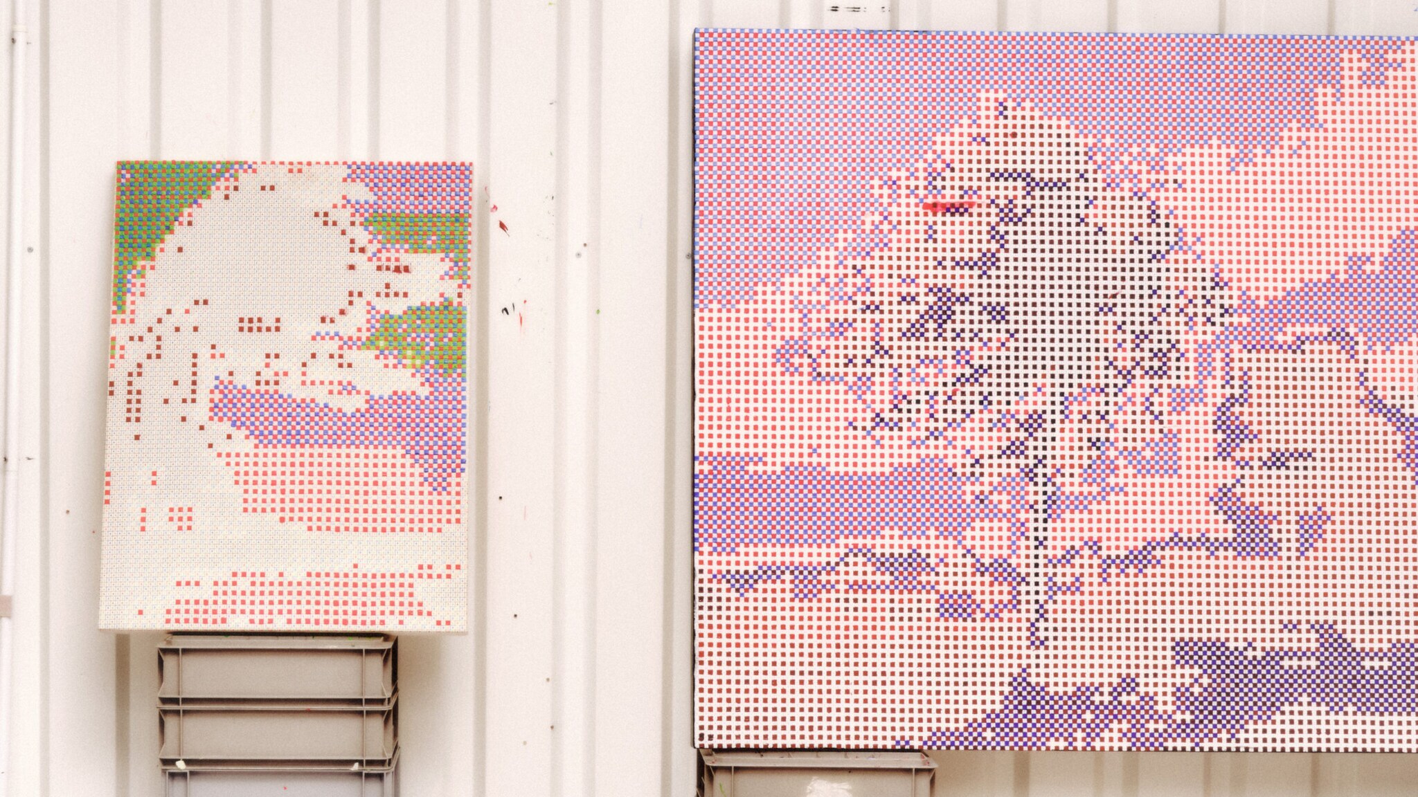 Zwei Kunstwerke auf Leinwänden mit gerasterten Mustern in Lilatönen lehnen an einer weißen Wand in einem Atelier.