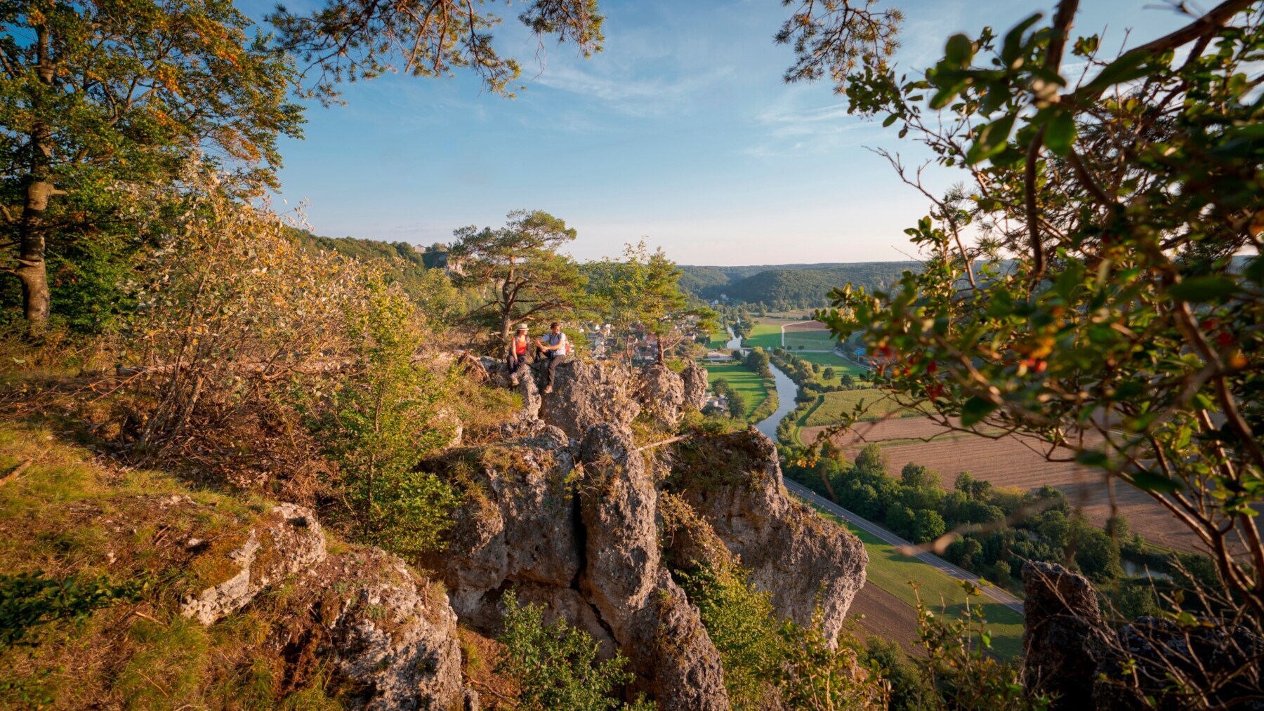 Zwei Wander:innen sitzen auf einem Felsen hoch über der Altmühl