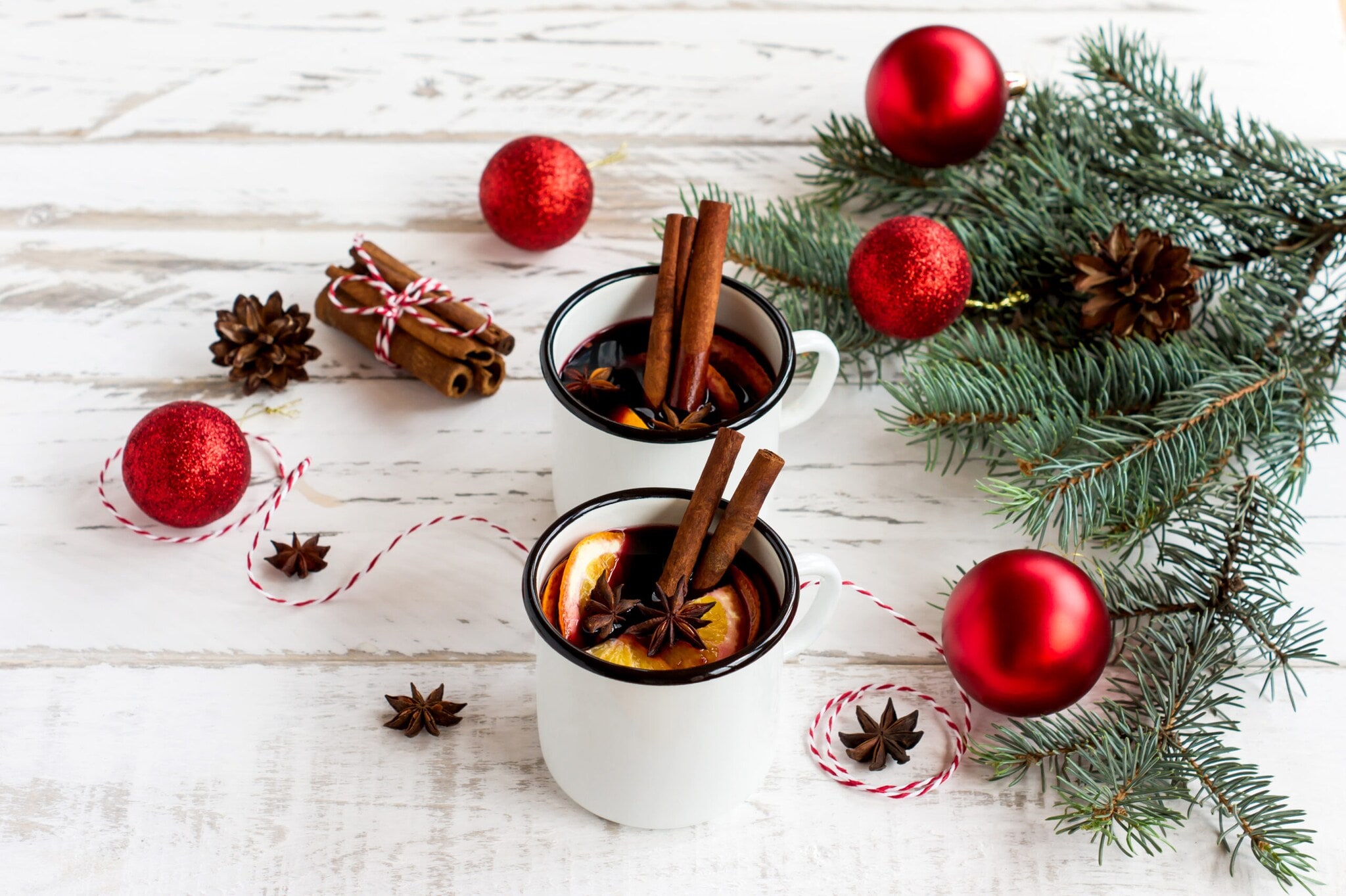 Heißgetränk in weiß emaillierten Bechern mit Gewürzen und Zitrusfrüchten Heißgetränk in weiß emaillierten Bechern mit Gewürzen und Zitrusfrüchten